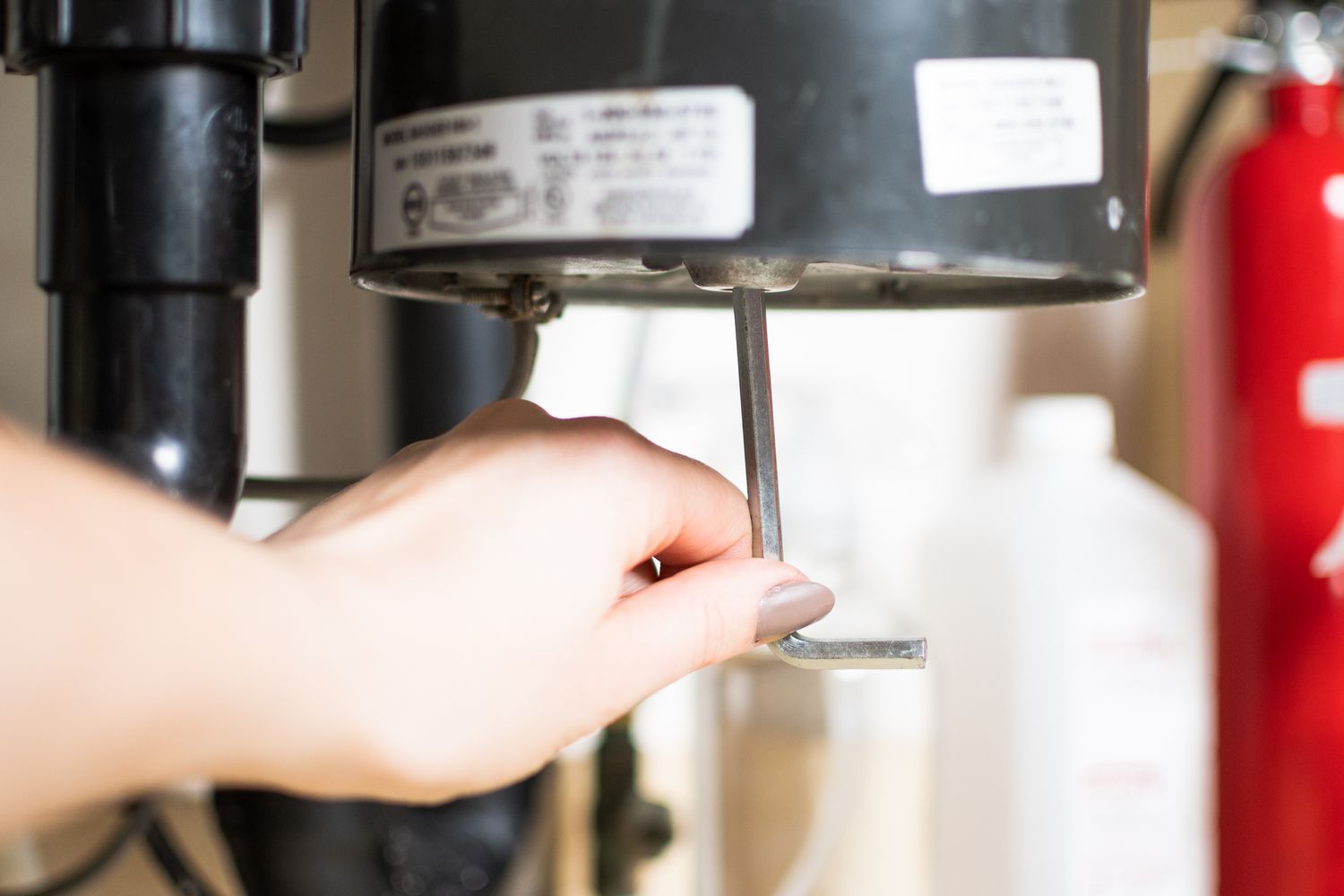 A 1/4-inch Allen wrench held next to the hex socket on the underside of a garbage disposal