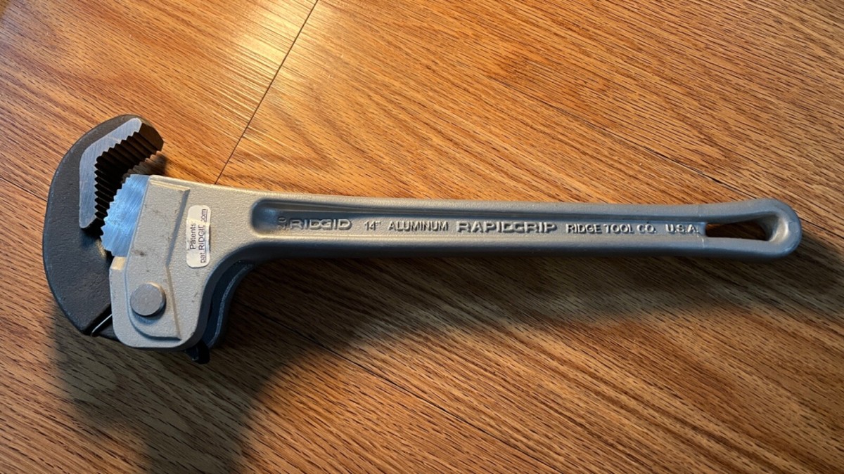 A 14-inch pipe wrench clamped onto a galvanized steel pipe fitting in a utility area