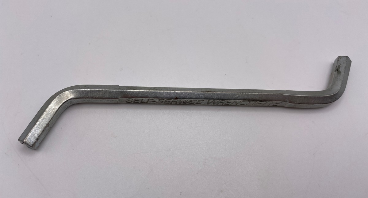 A Jam-Buster style garbage disposal wrench inserted into the sink opening and engaged with the disposal turning lugs