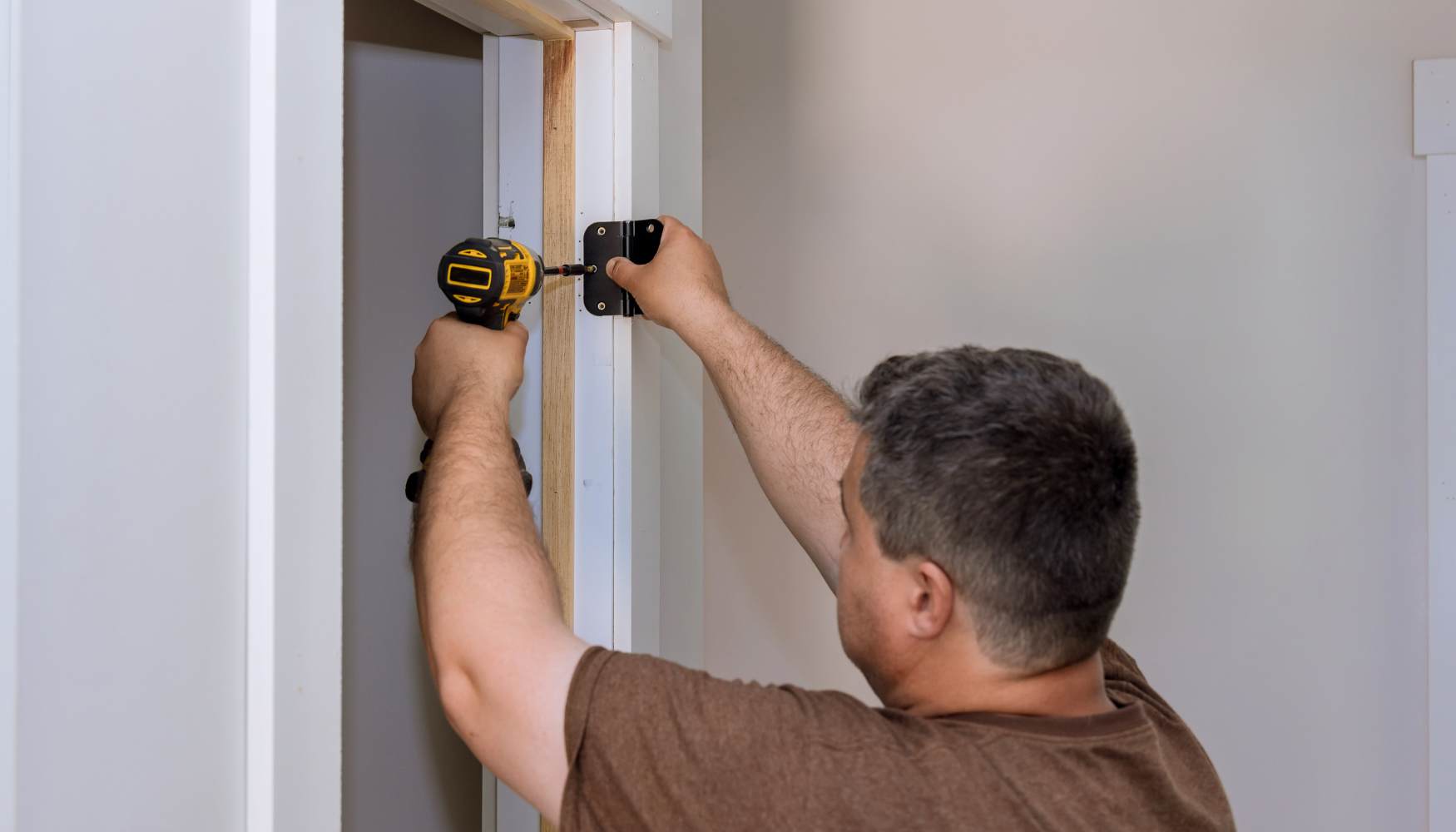 A bar clamp spanning a door jamb on the latch side, with small wood blocks placed under the clamp pads to protect the trim and jamb surface