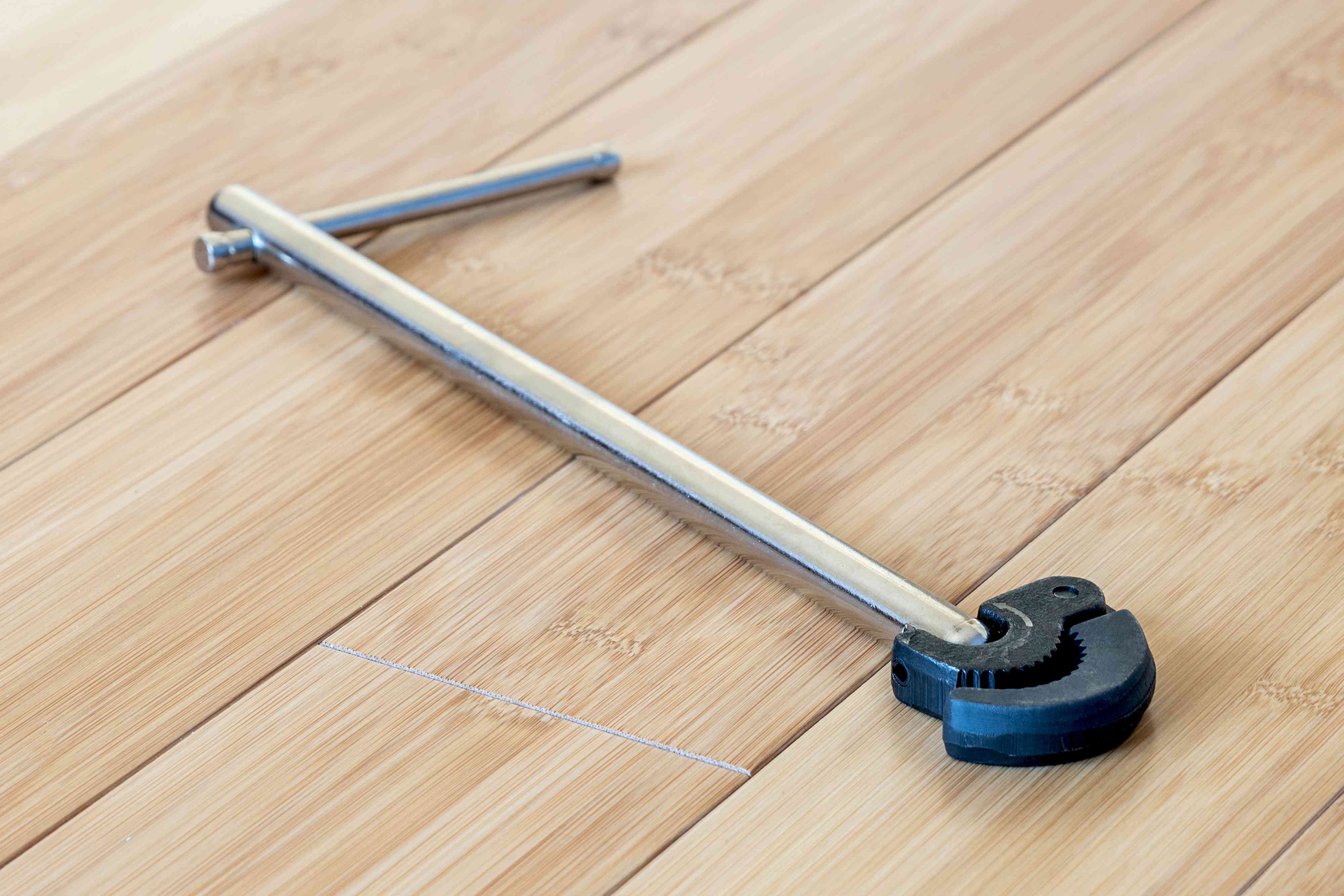 A basin wrench positioned up under a bathroom sink, gripping the hard-to-reach mounting nut of a faucet