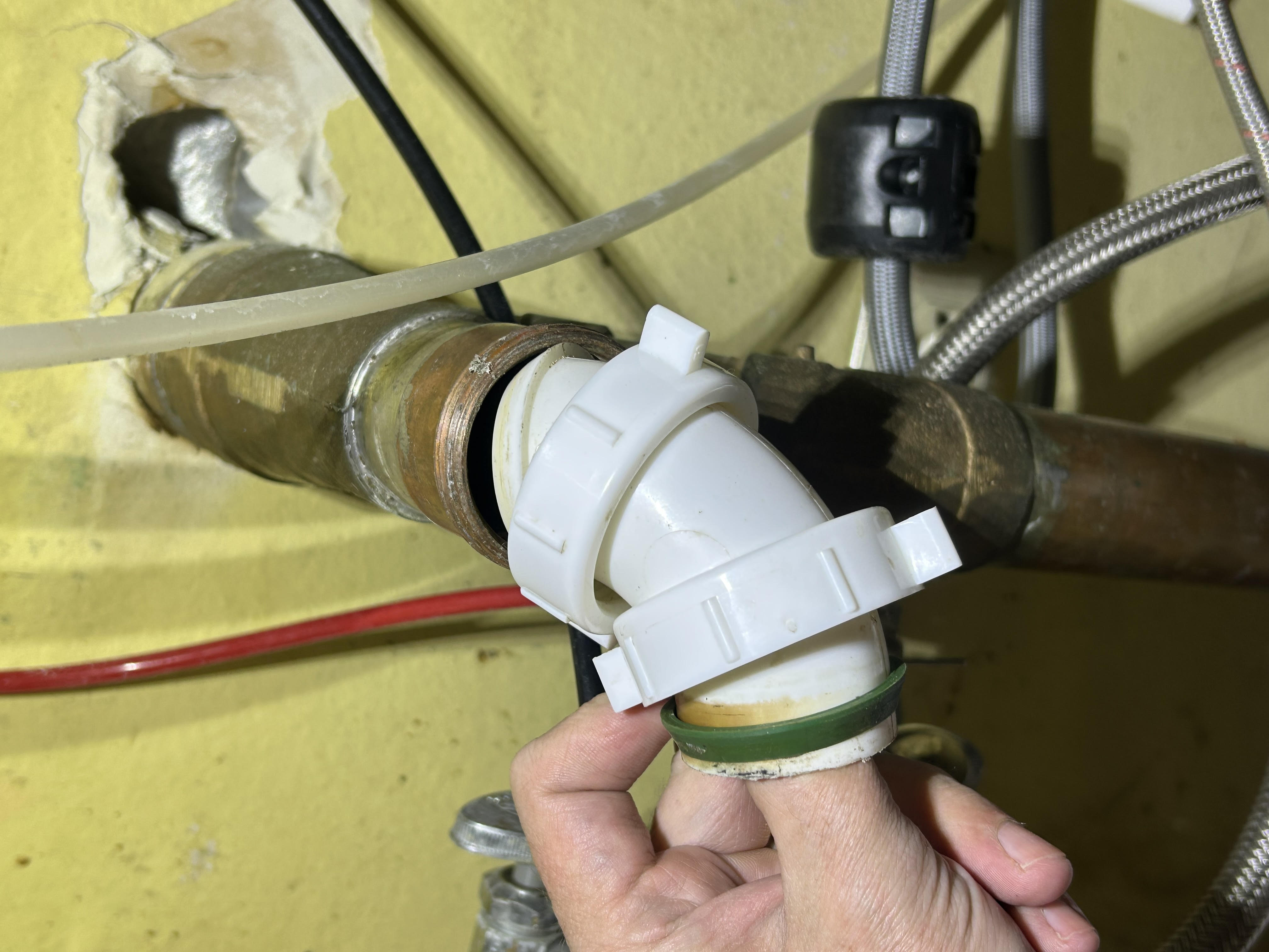A beveled plastic slip-joint washer resting on a homeowner's palm next to a PVC slip nut under a sink