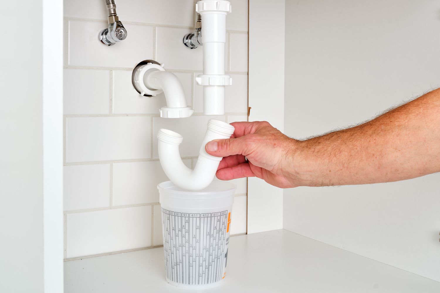 A bucket placed under a kitchen sink P-trap while slip nuts are being loosened by hand