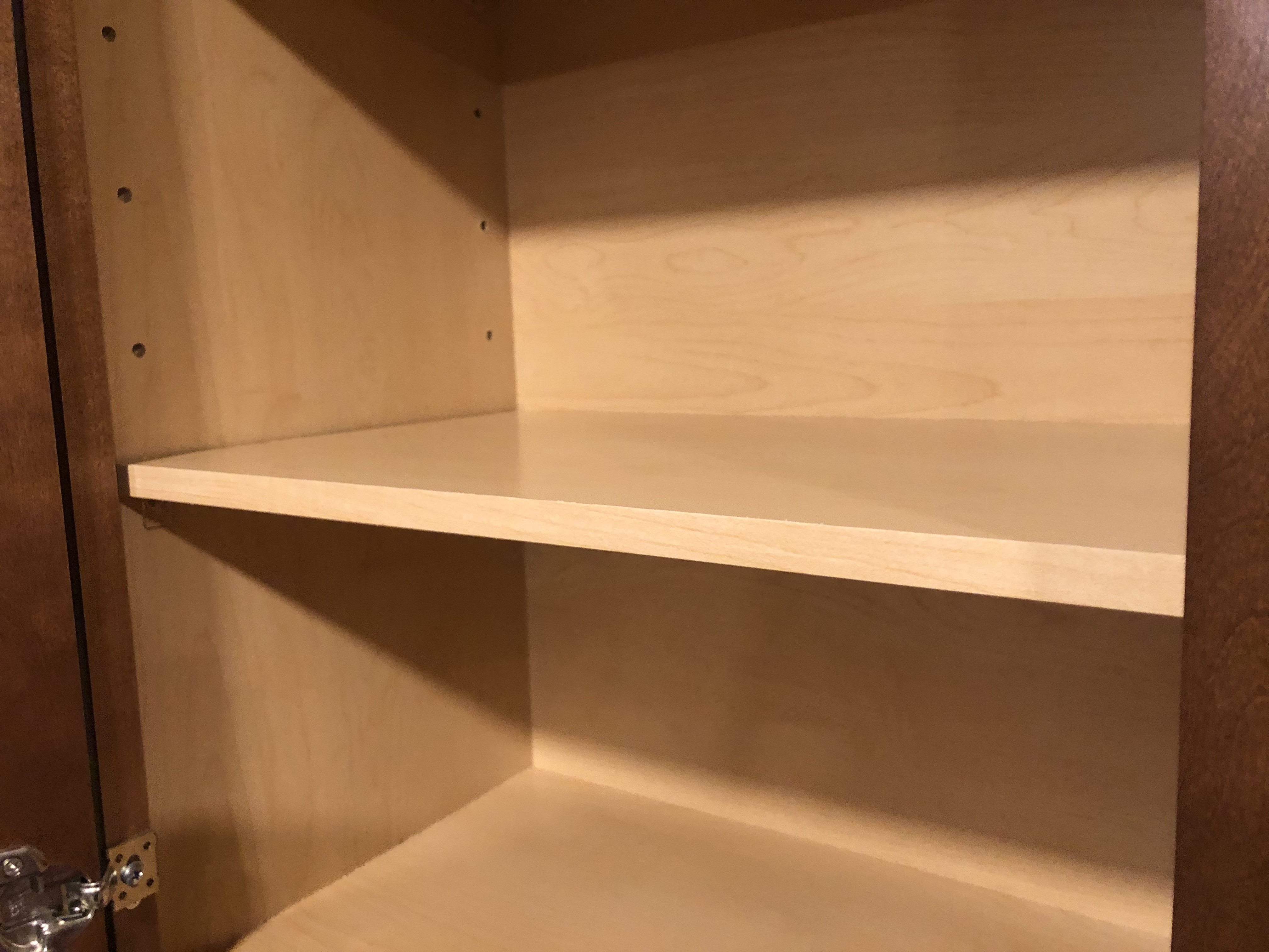 A cabinet shelf on a workbench with a hardwood strip clamped along the front edge, with glue squeeze-out visible at the seam