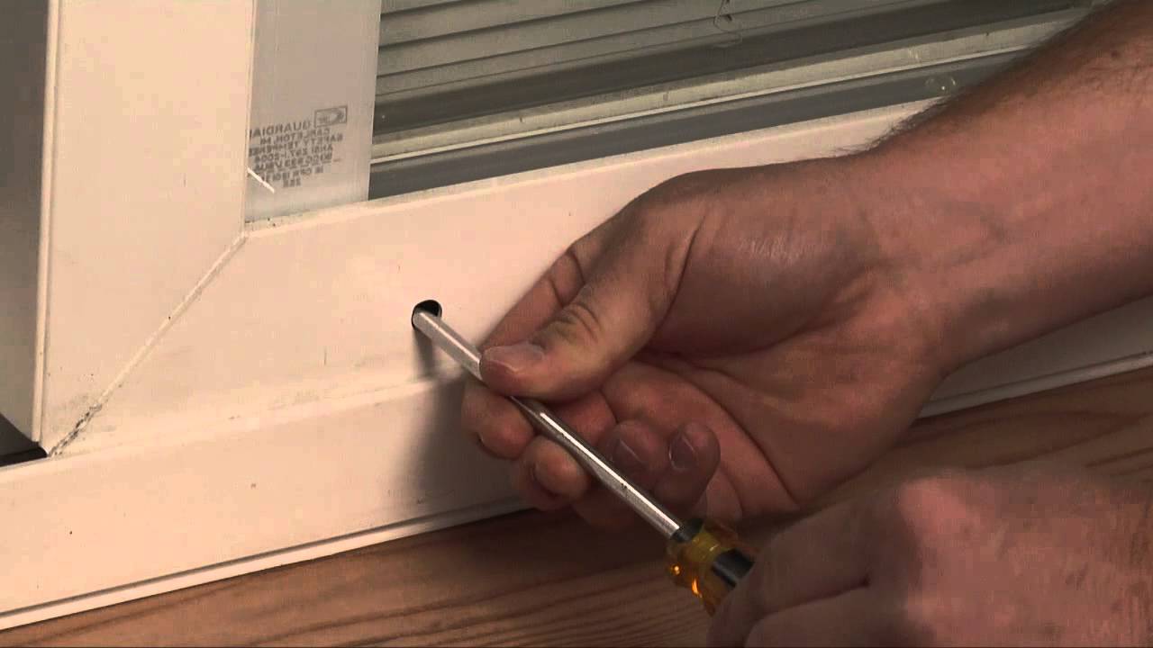 A close-up of a hand turning a screwdriver in the roller adjustment screw at the bottom corner of a sliding glass door