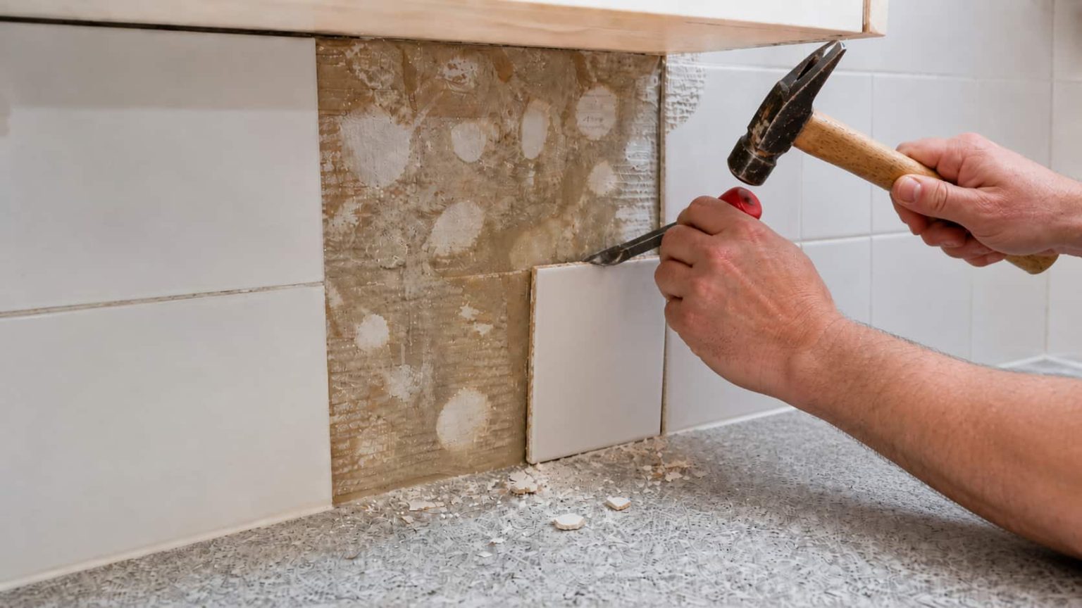 A cold chisel and hammer breaking a ceramic tile at the center so pieces lift out safely
