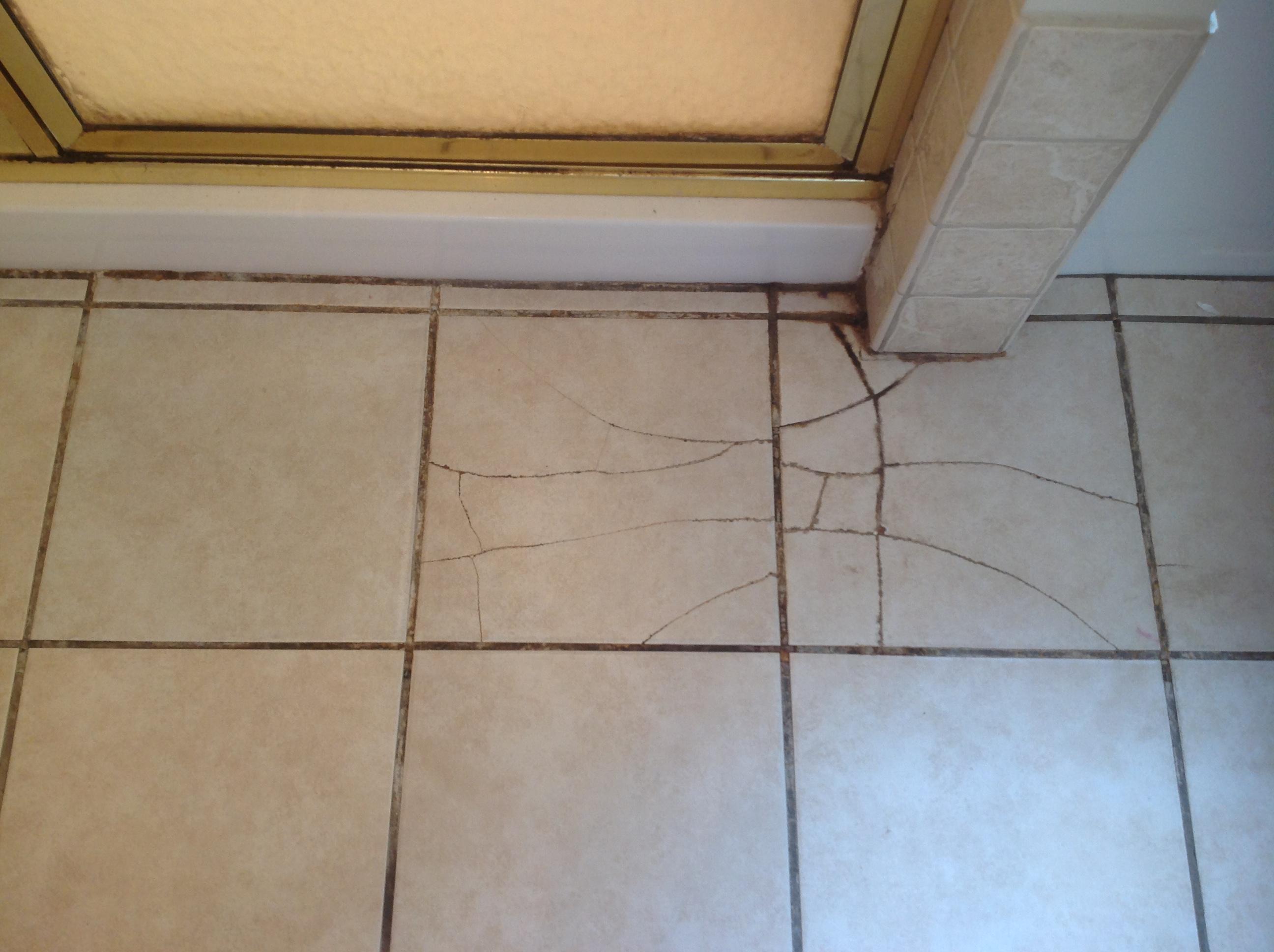 A cracked ceramic bathroom floor tile with intact grout joints around it