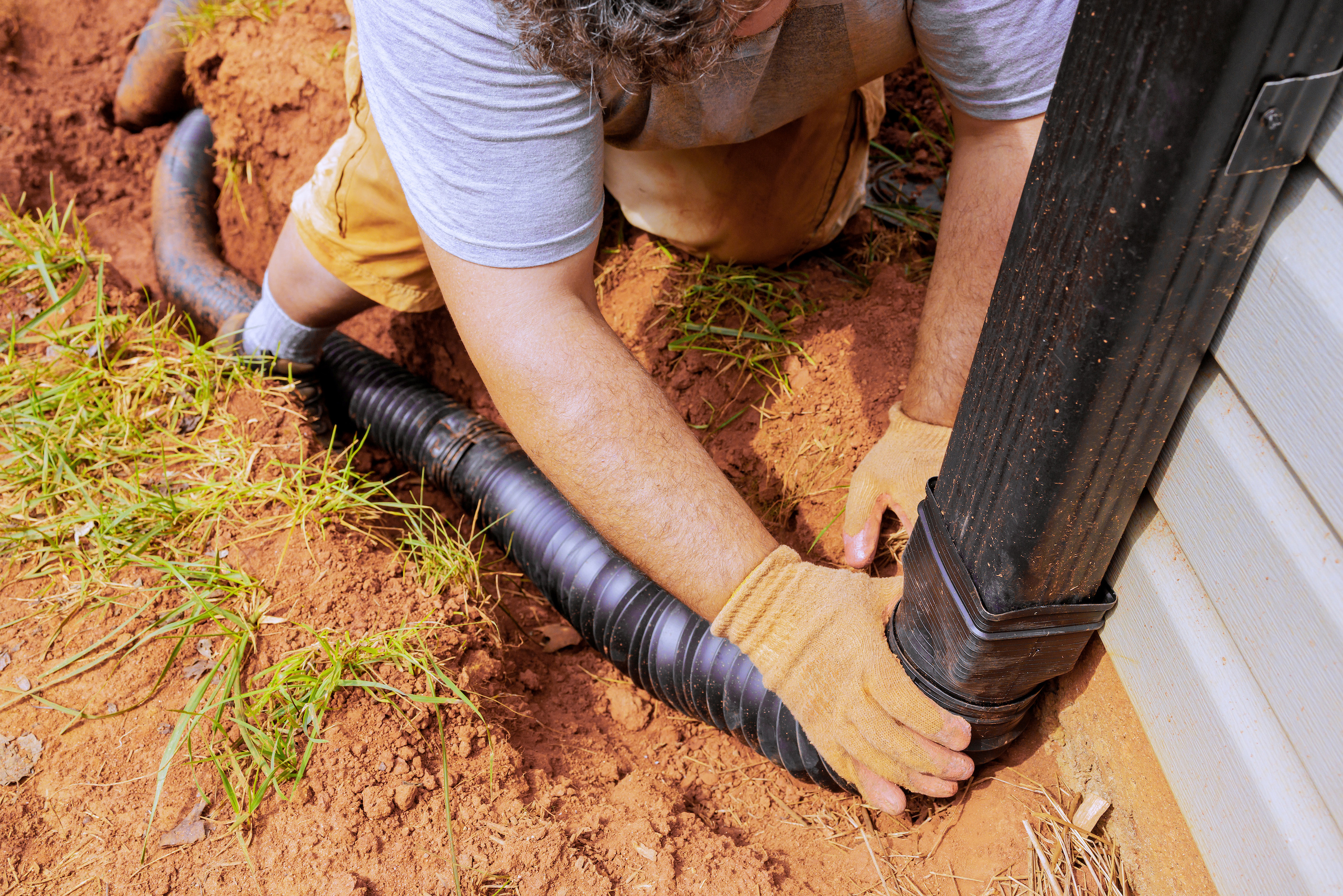 A downspout extension carrying roof runoff away from the foundation along a yard that slopes away from the house