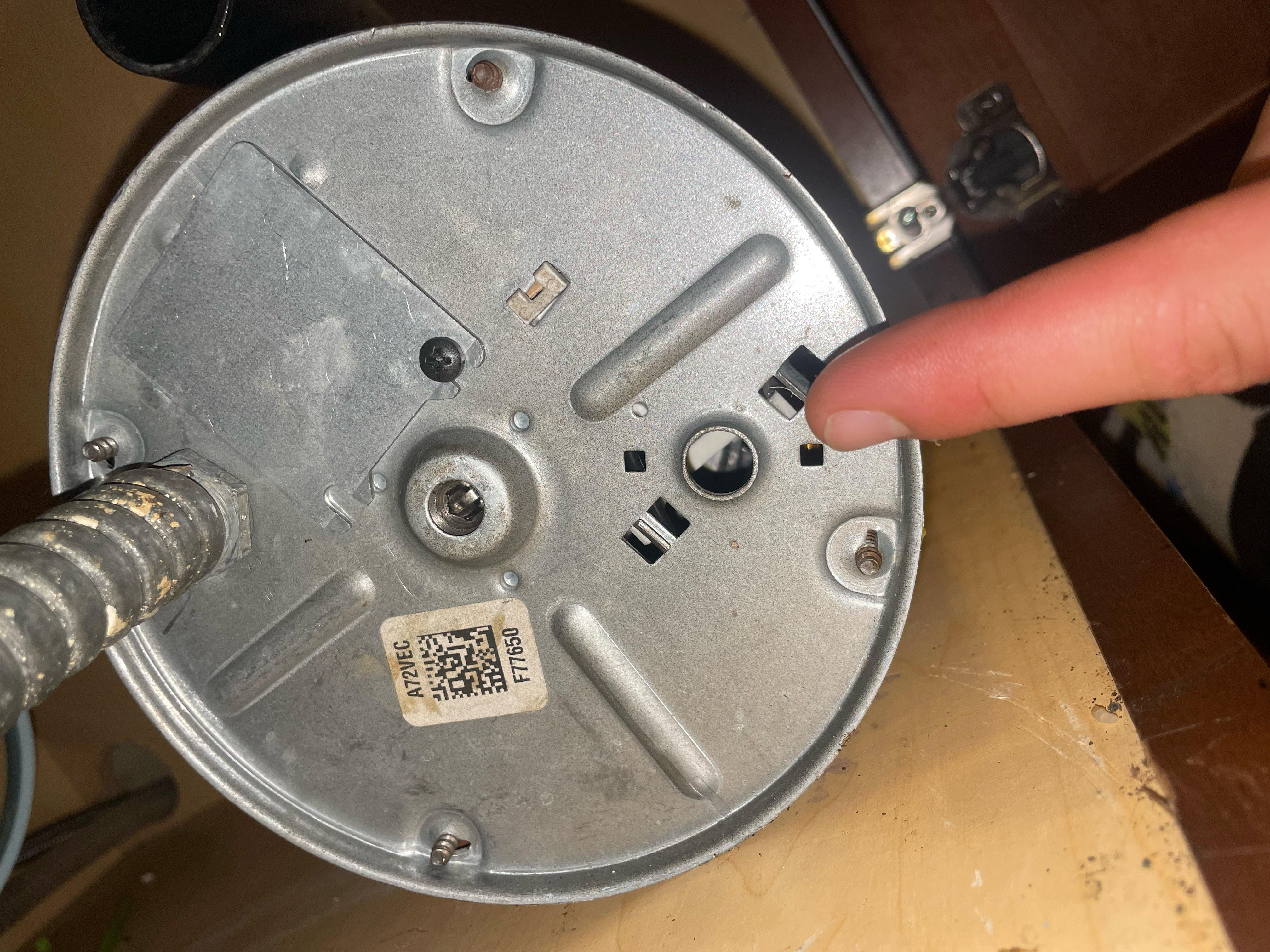 A finger pressing the small round reset button on the bottom of a garbage disposal