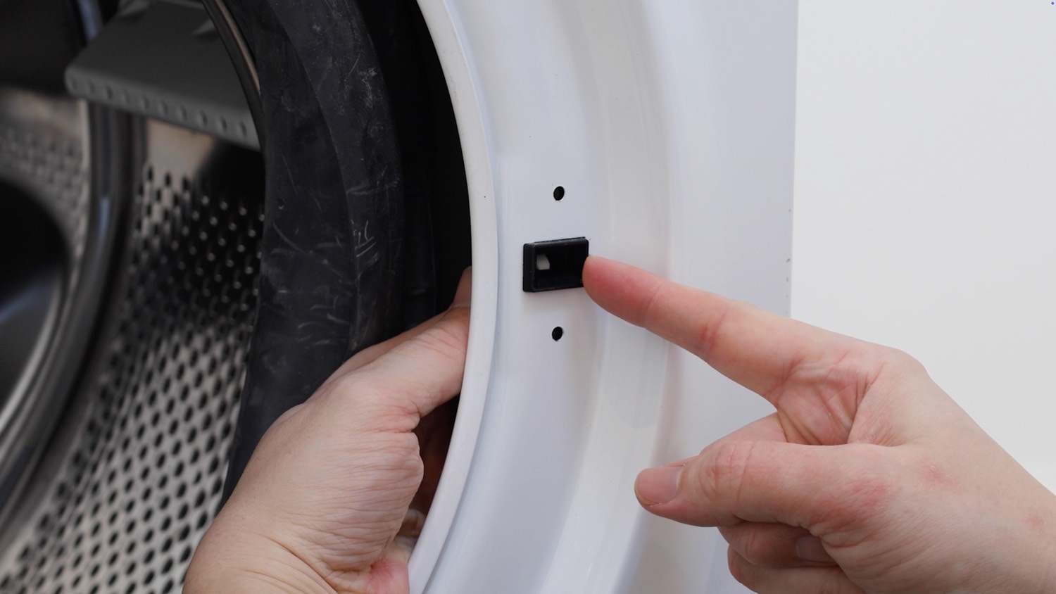 A front-load washer door slightly open, showing the door latch and strike alignment at the lock mechanism