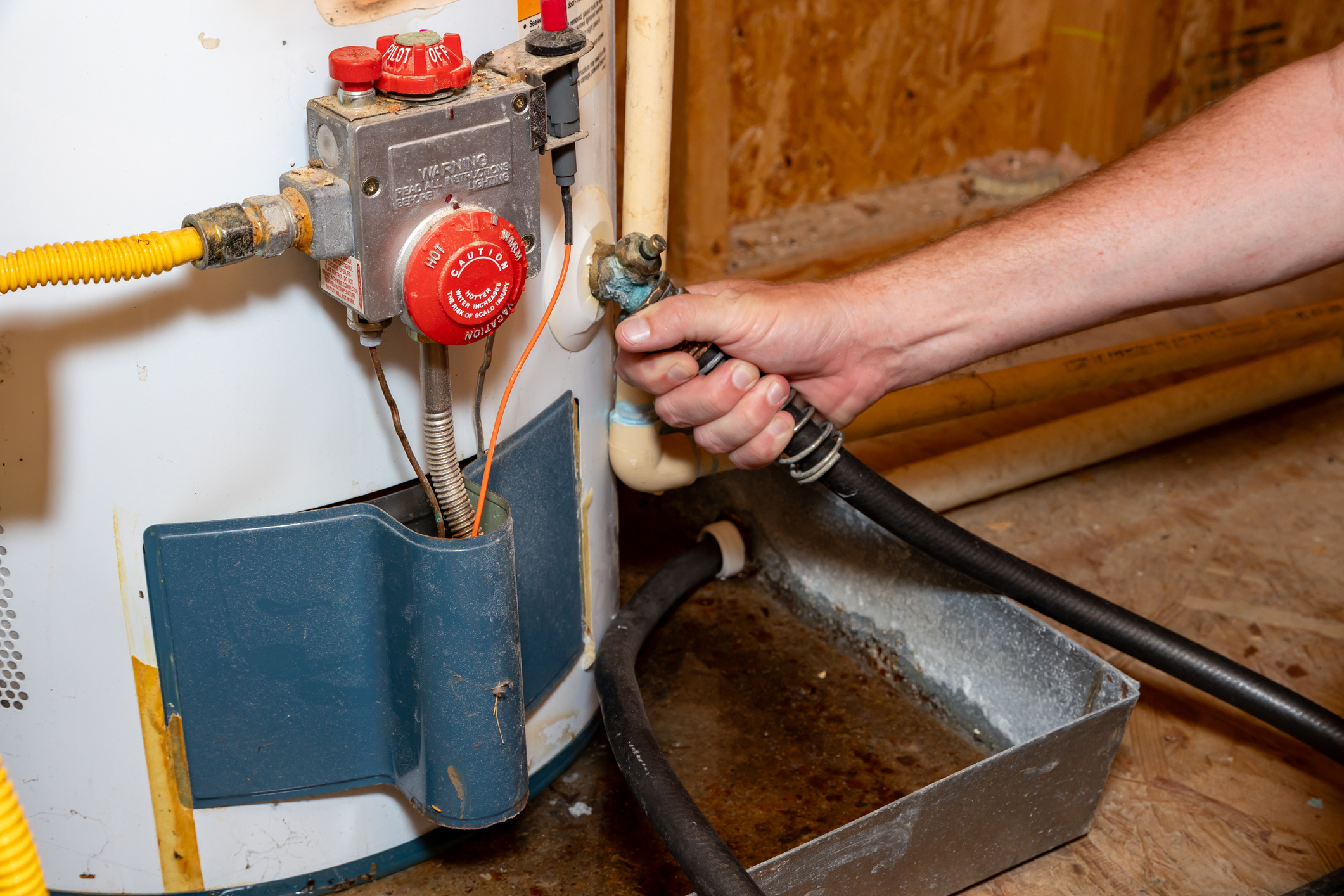 A garden hose attached to a water heater drain valve, with the hose leading to a floor drain