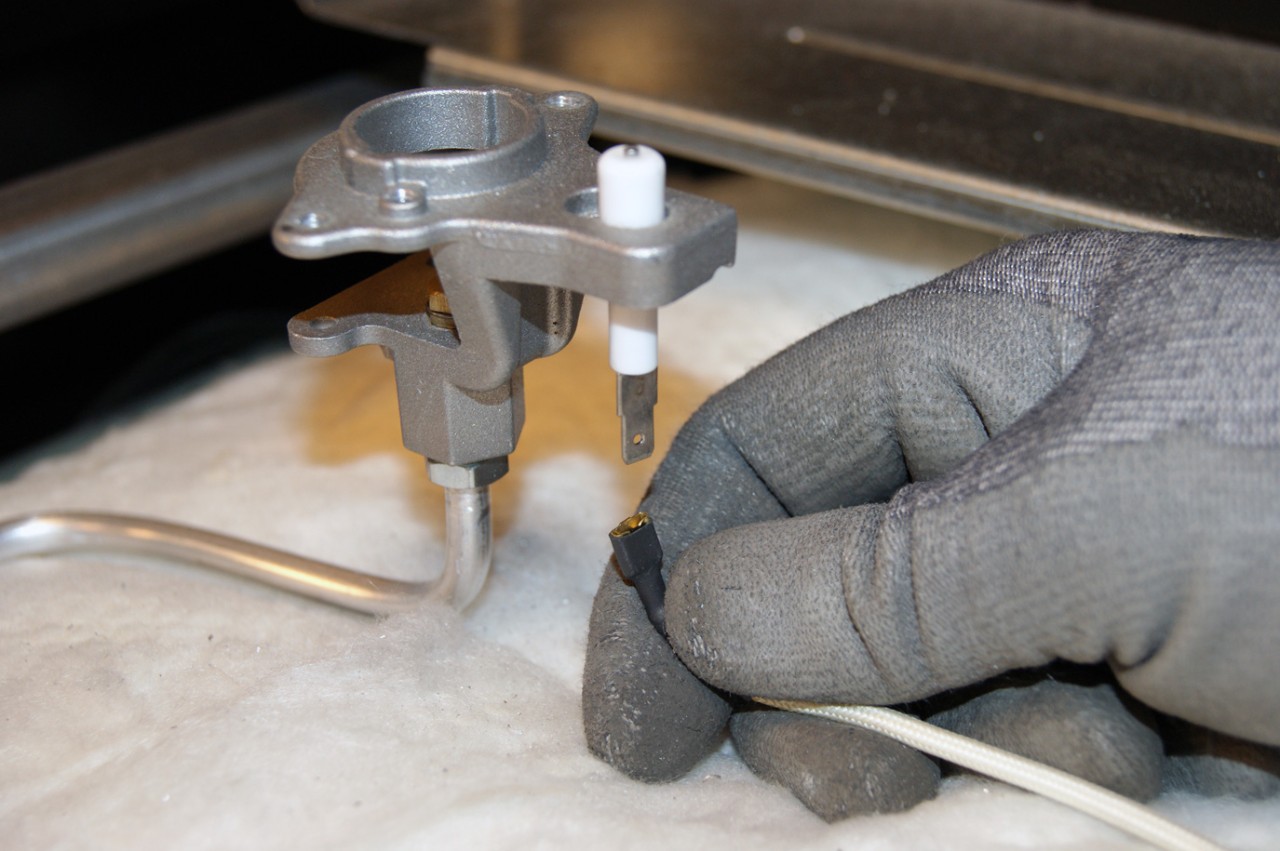 A gas stove spark igniter electrode with a visible crack in the white ceramic insulator near the metal tip