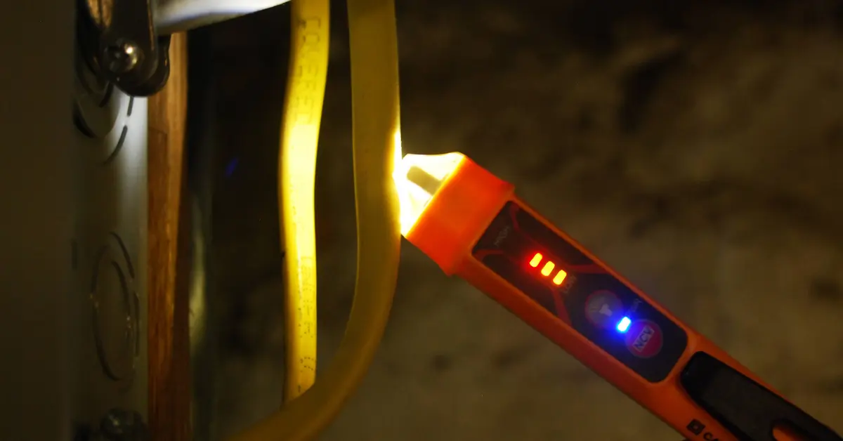 A hand holding a non-contact voltage tester near a wall outlet cover plate during a safety check