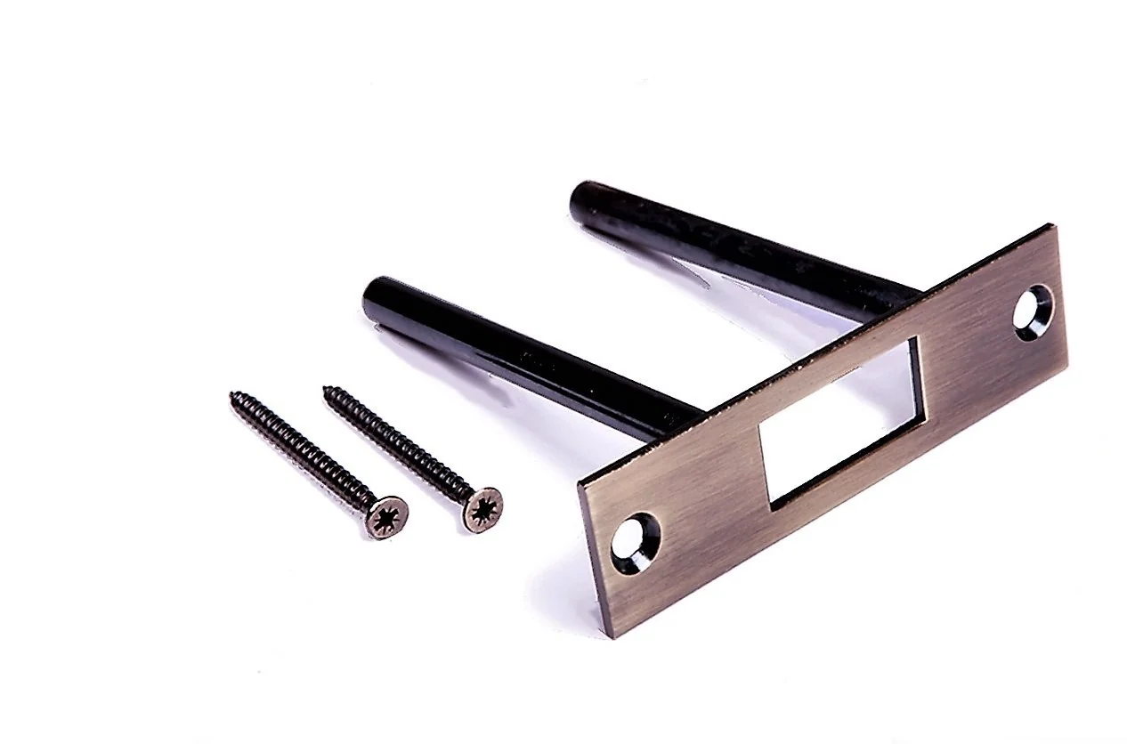 A hand using a flat metal file on a door strike plate opening while the plate is held steady on a workbench