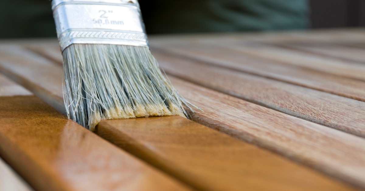 A hand wearing a nitrile glove brushing liquid wood hardener into a cleaned-out window sill cavity