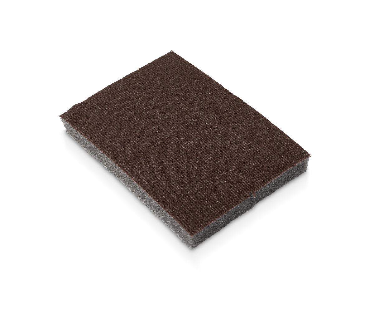 A metal paint scraper and sanding sponge resting on a drop cloth next to a small pile of scraped paint chips