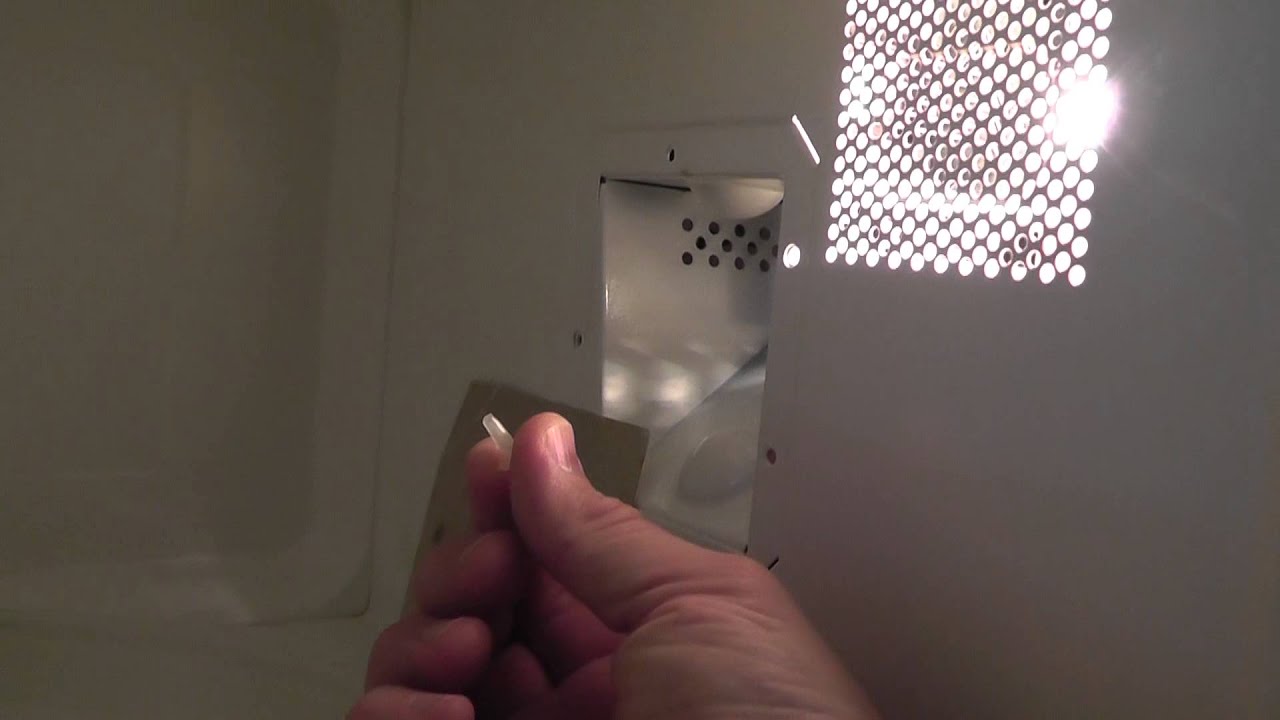 A person aligning a new waveguide cover inside a microwave, holding it flat against the side wall before fastening it