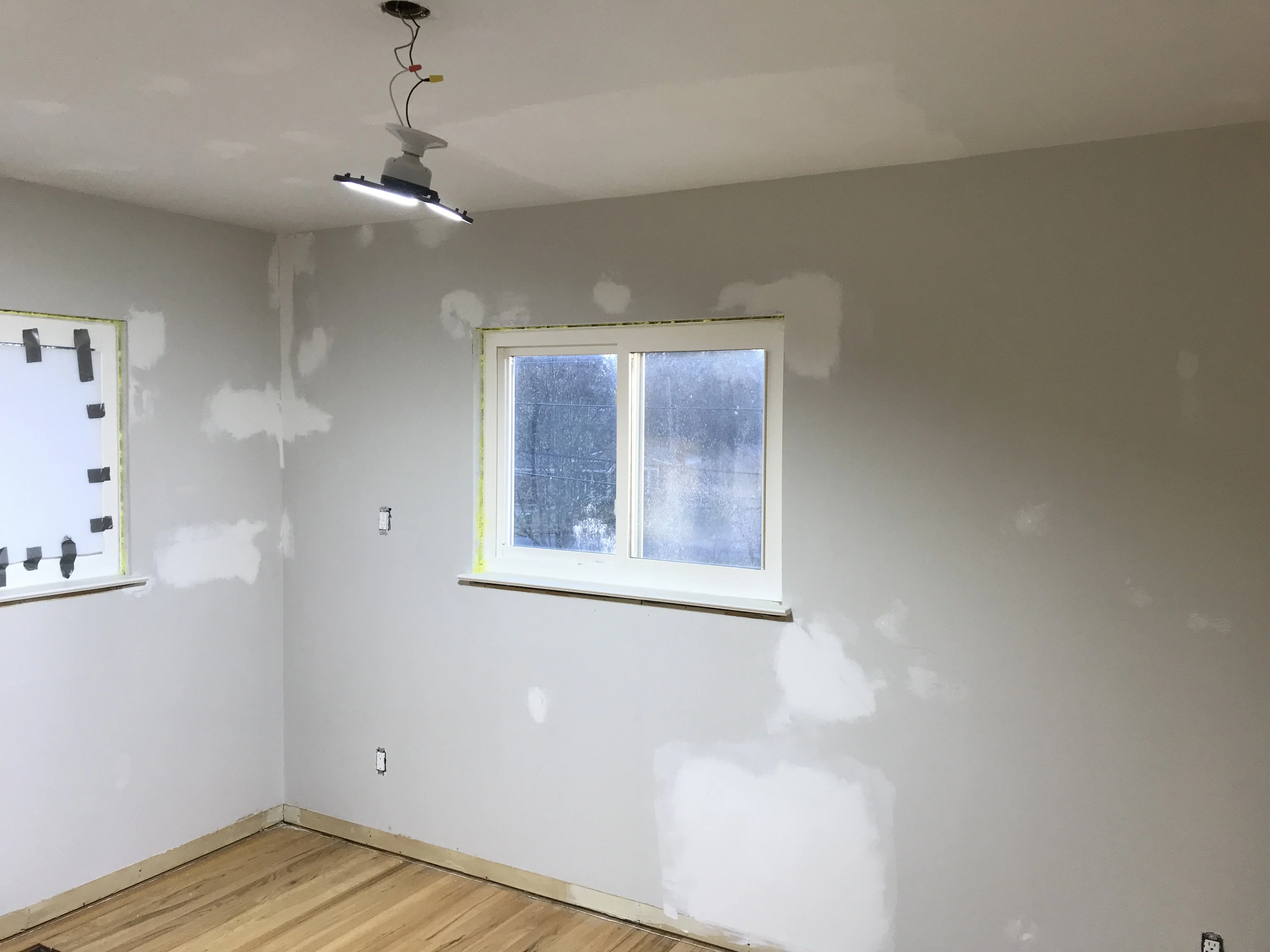 A person using a paint roller to apply white primer over a sanded drywall repair area on an interior wall