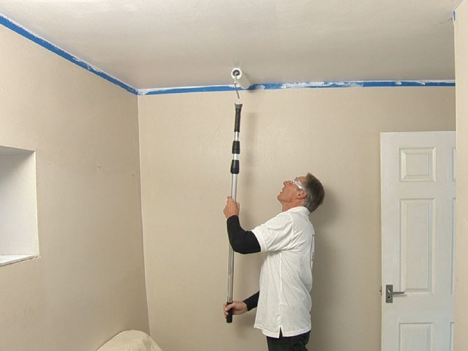A person using a roller on an extension pole to apply flat white paint across a residential ceiling