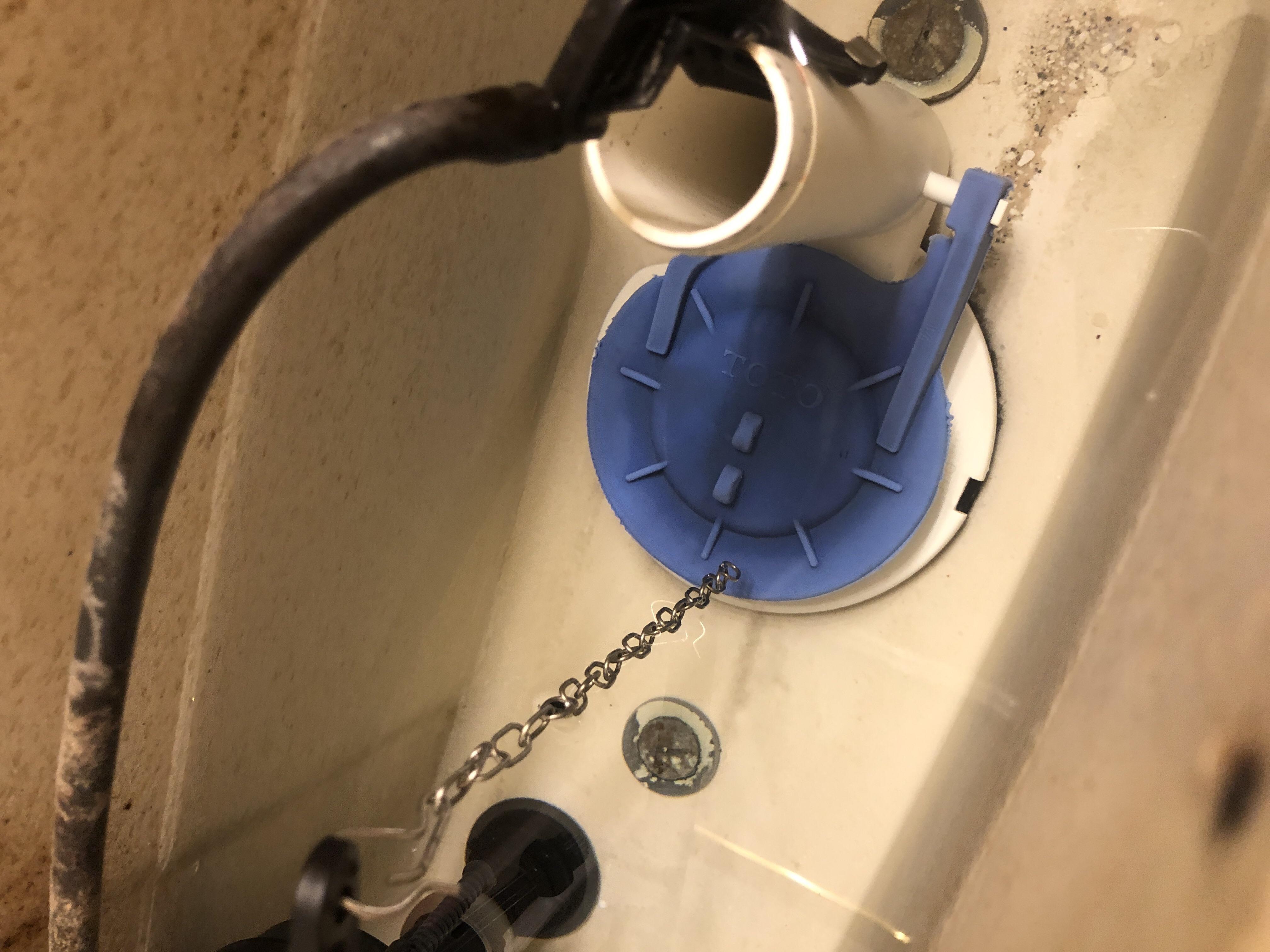 A real close-up photo of a toilet flapper chain connected to the flush handle arm with slight slack while the flapper sits closed