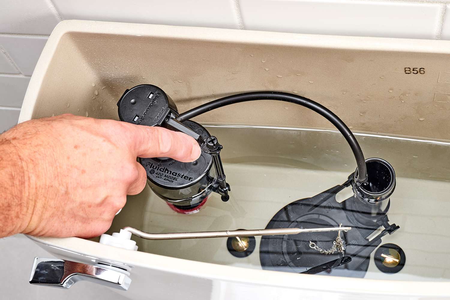 A real photo close-up of a modern toilet fill valve with a float cup and an adjustment screw inside an open toilet tank