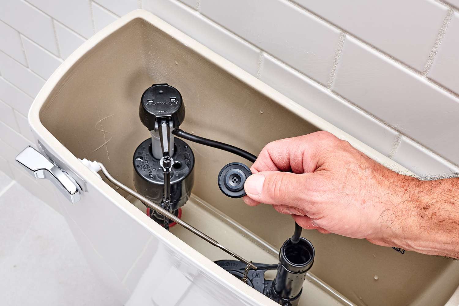 A real photo of hands using an adjustable wrench to loosen the locknut under a toilet tank while the tank lid is off