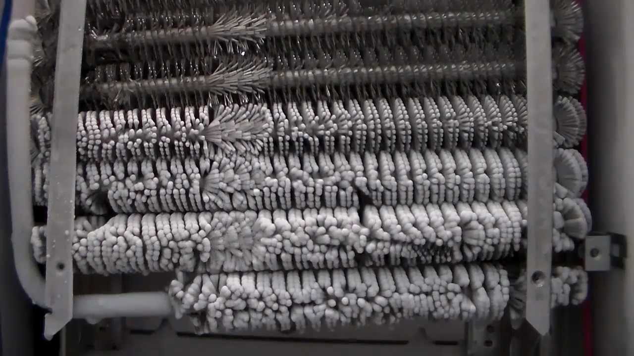 A refrigerator evaporator coil behind the freezer panel heavily coated in white frost and ice, blocking airflow