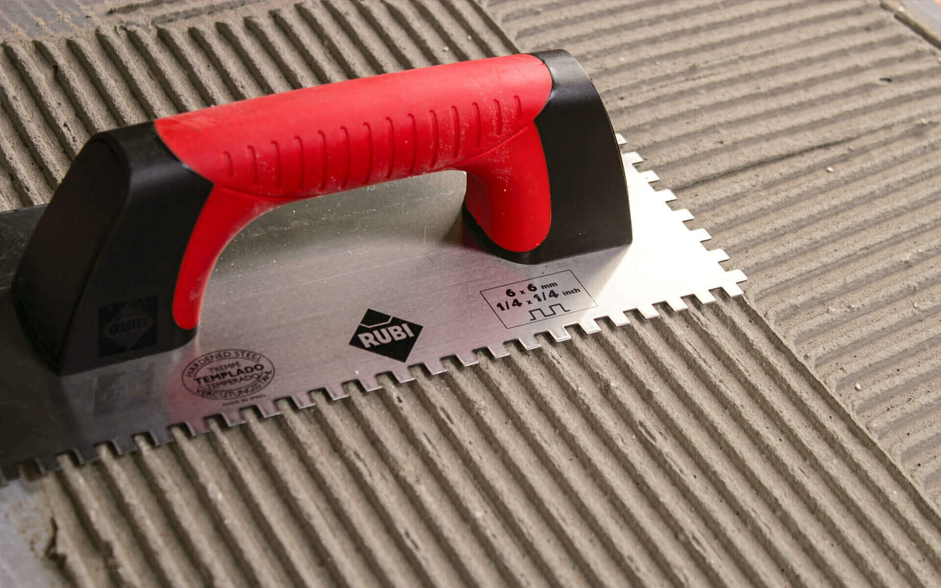 A replacement tile being pressed into fresh mortar combed with a notched trowel