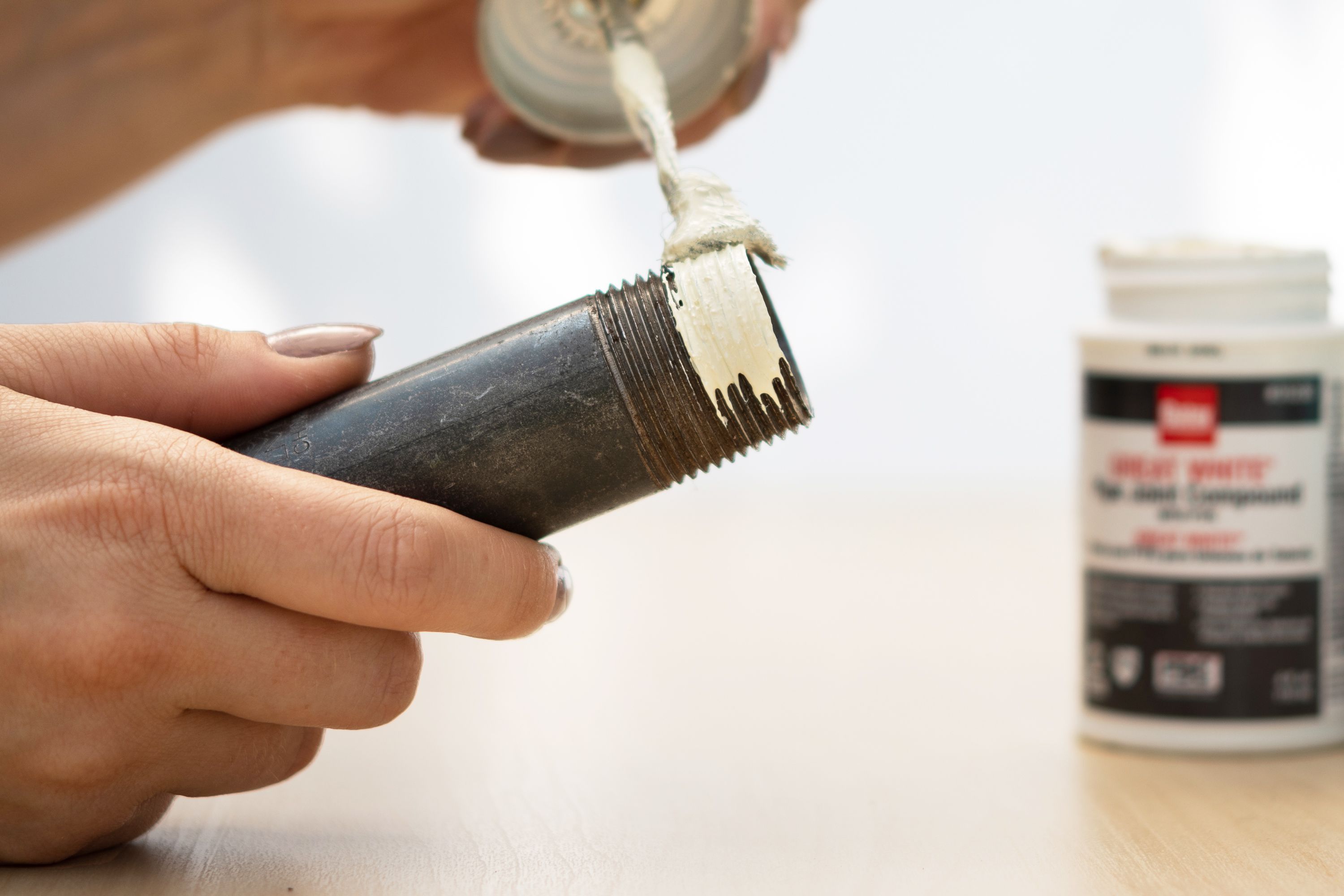A roll of white PTFE thread seal tape and a small container of pipe joint compound on a workbench