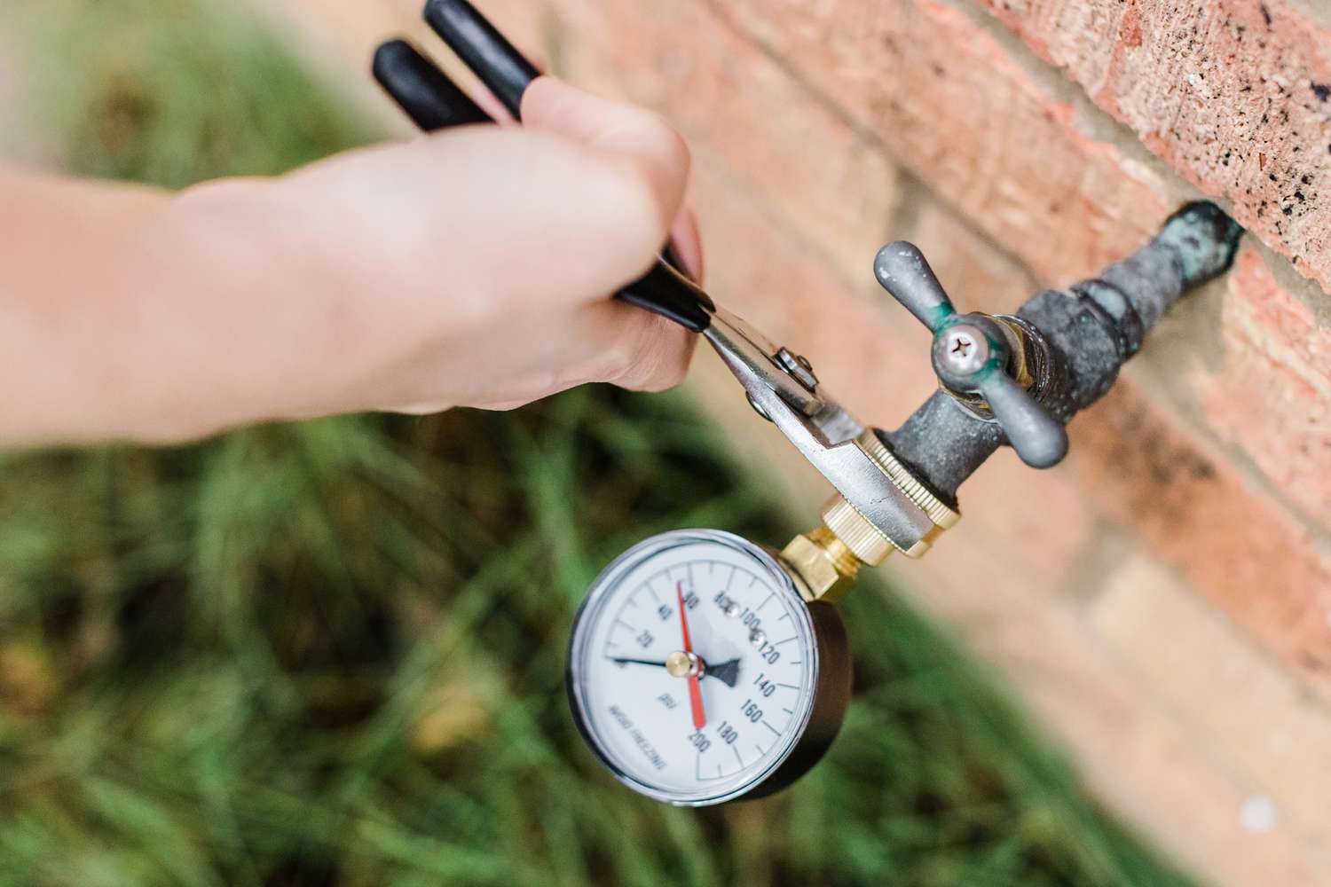 A round water pressure gauge threaded onto an outdoor hose bib, showing a PSI reading