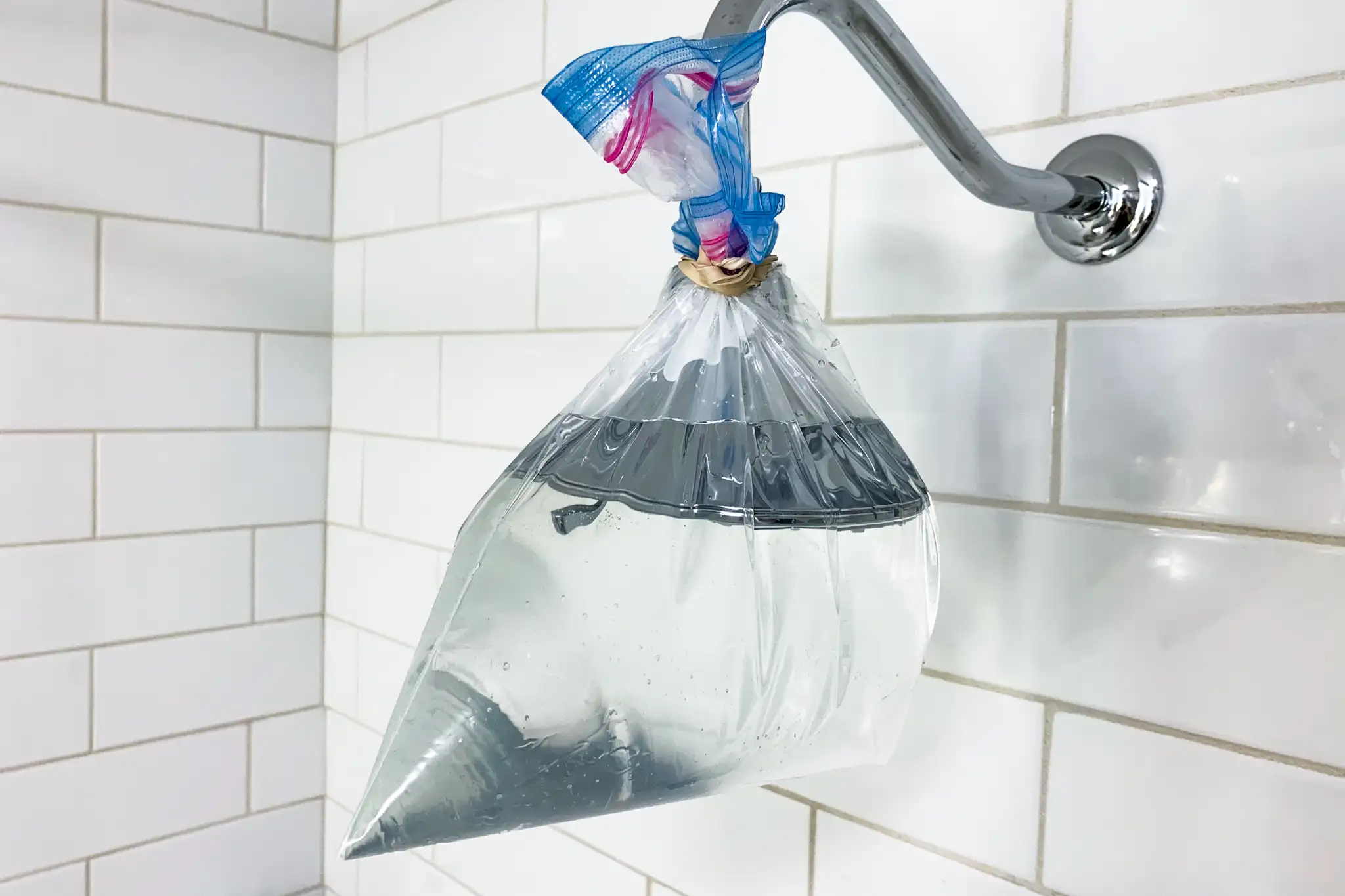 A showerhead wrapped with a plastic bag filled with white vinegar and secured with a rubber band for descaling