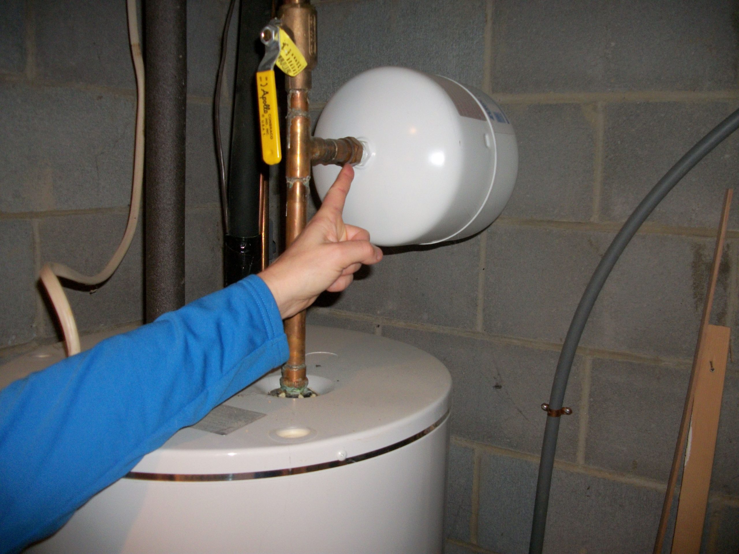 A small metal thermal expansion tank mounted above a residential water heater on a copper cold water line