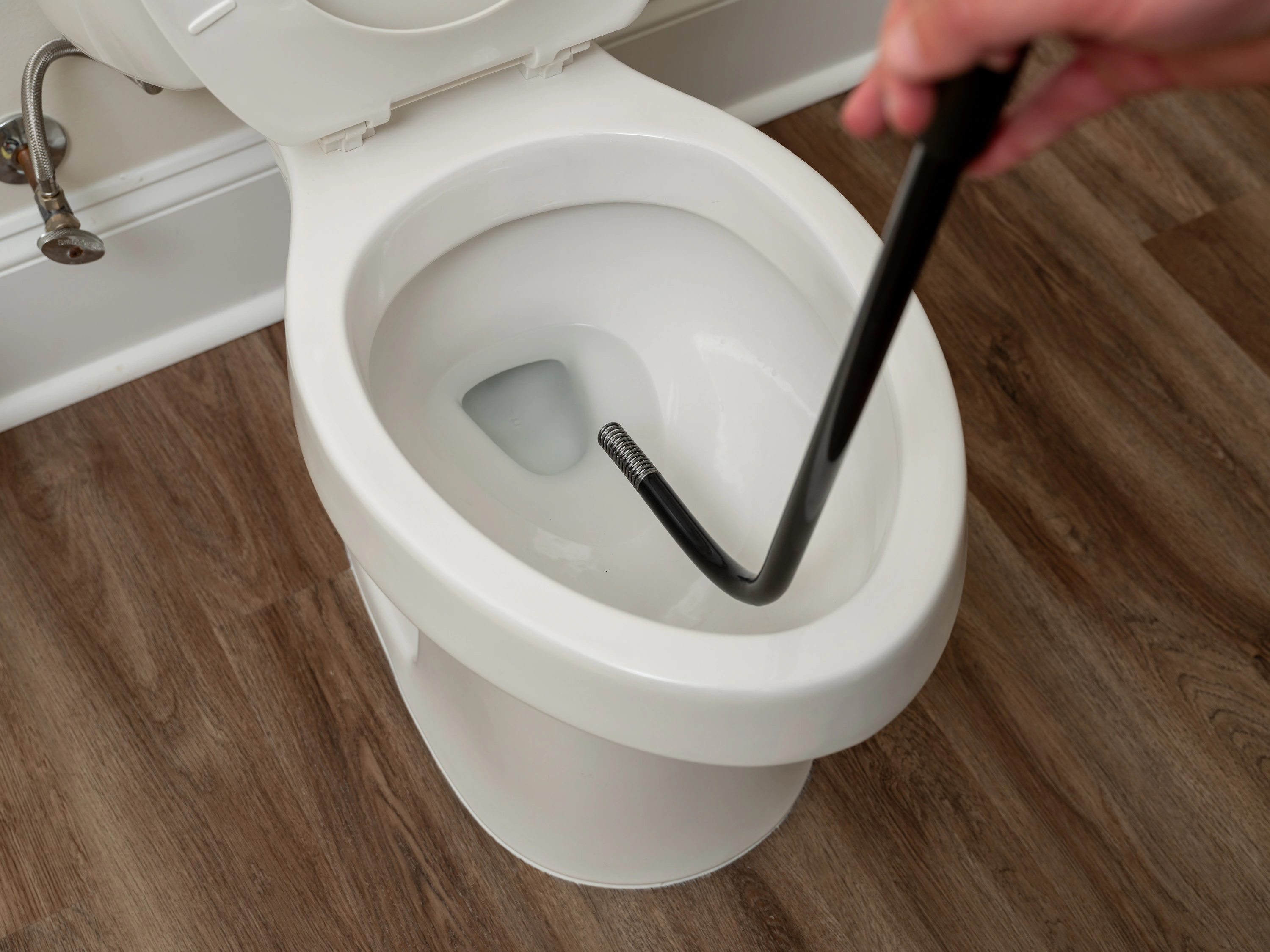 A toilet auger cable extended into a toilet bowl with the handle held above the rim