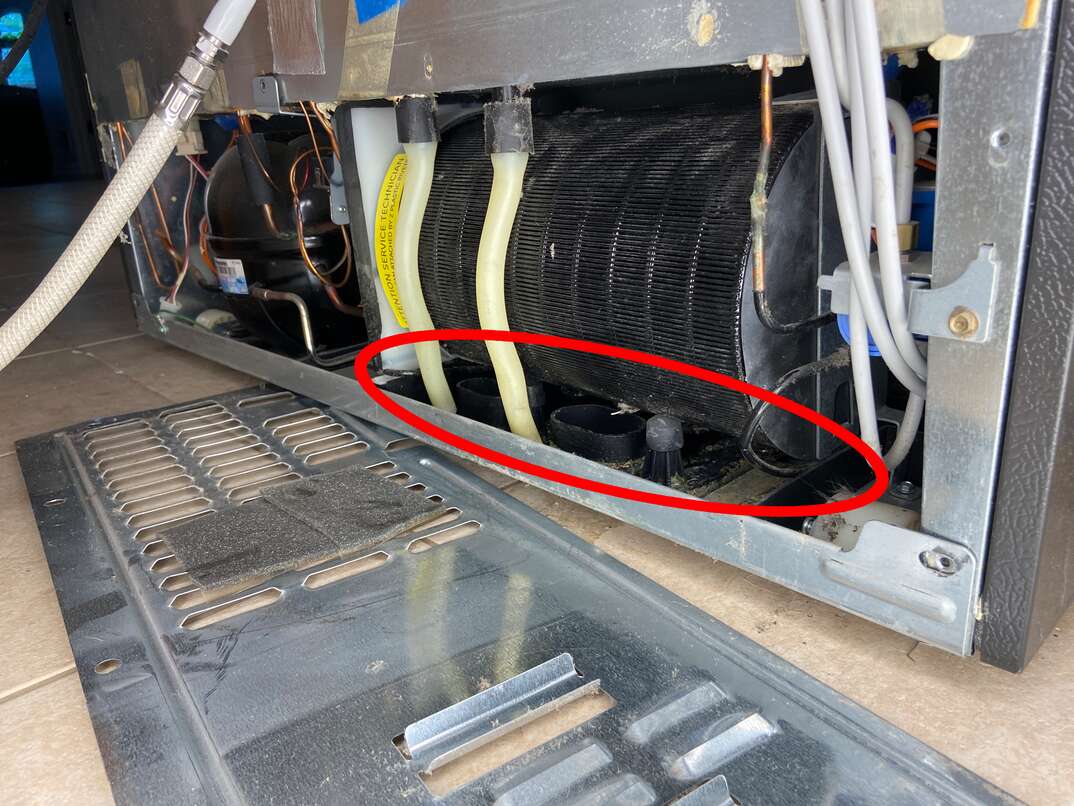 A view behind the lower rear panel of a refrigerator showing the plastic drain pan beneath the compressor area