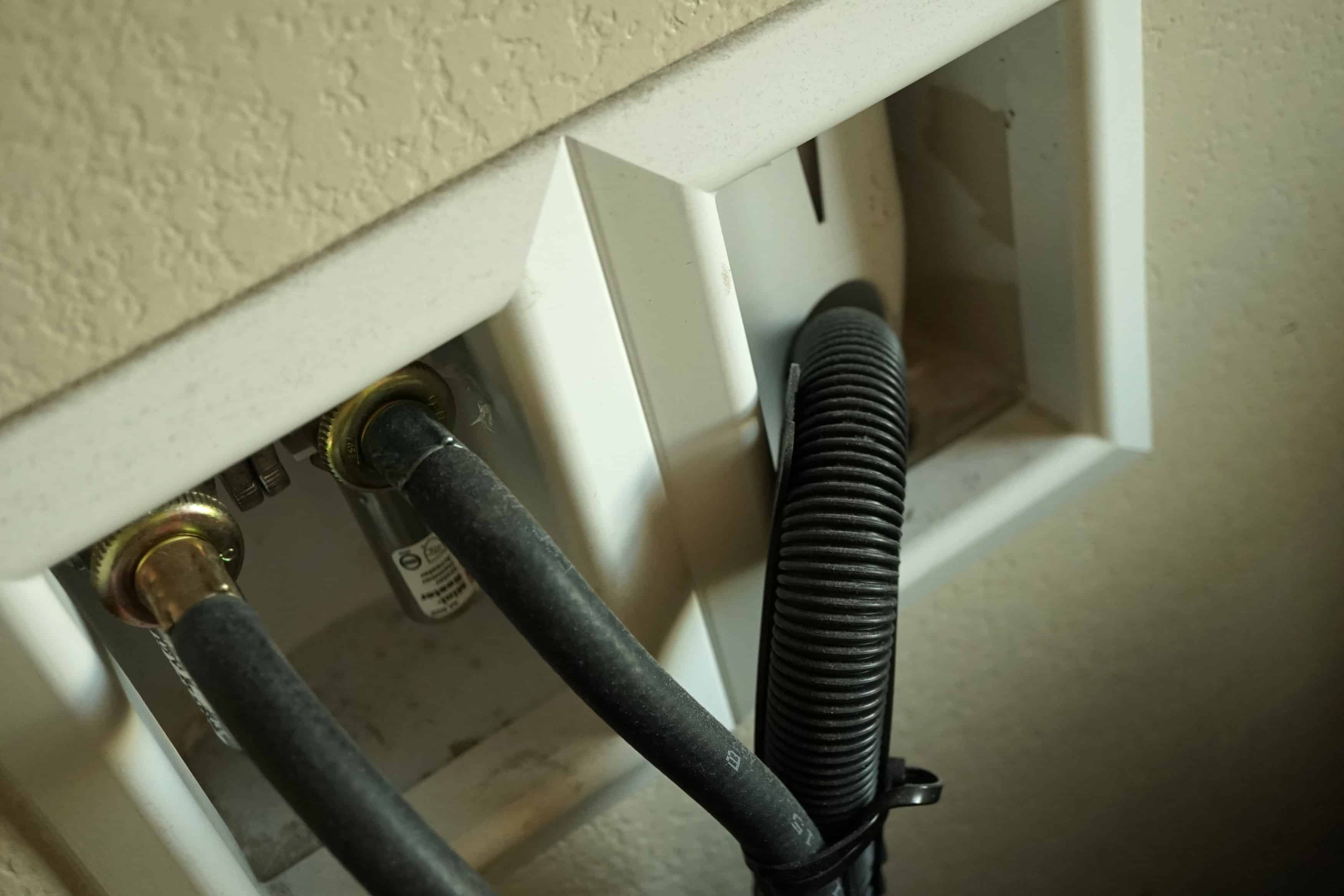 A washing machine drain hose bent sharply behind the appliance, showing a kinked section that could restrict water flow