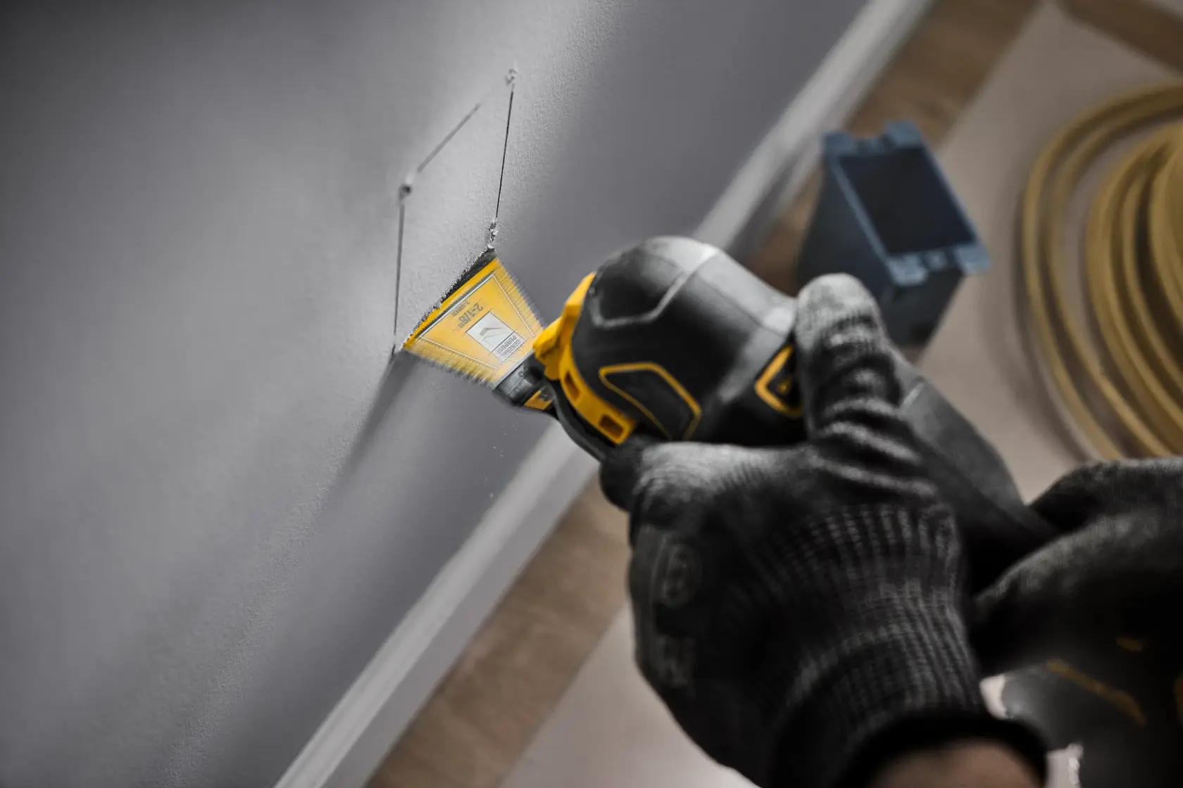 An oscillating multi-tool cutting a straight line in drywall along a pencil mark, with drywall dust falling