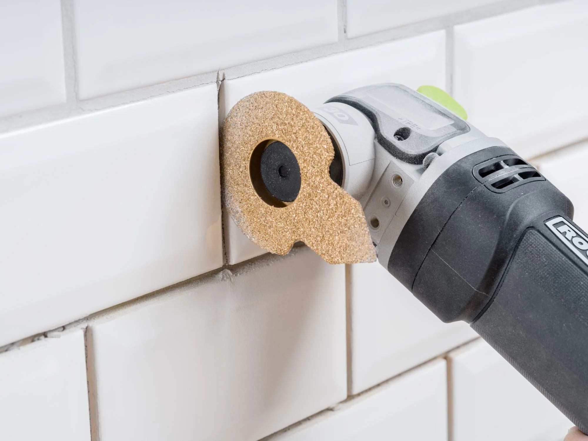 An oscillating multi-tool fitted with a grout removal blade next to a tiled surface