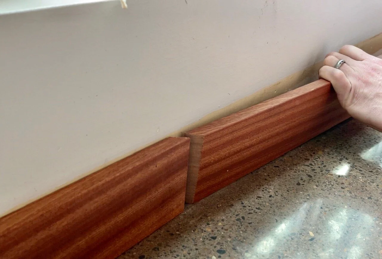 An oscillating multi-tool making a square cut through a painted baseboard to remove a damaged section