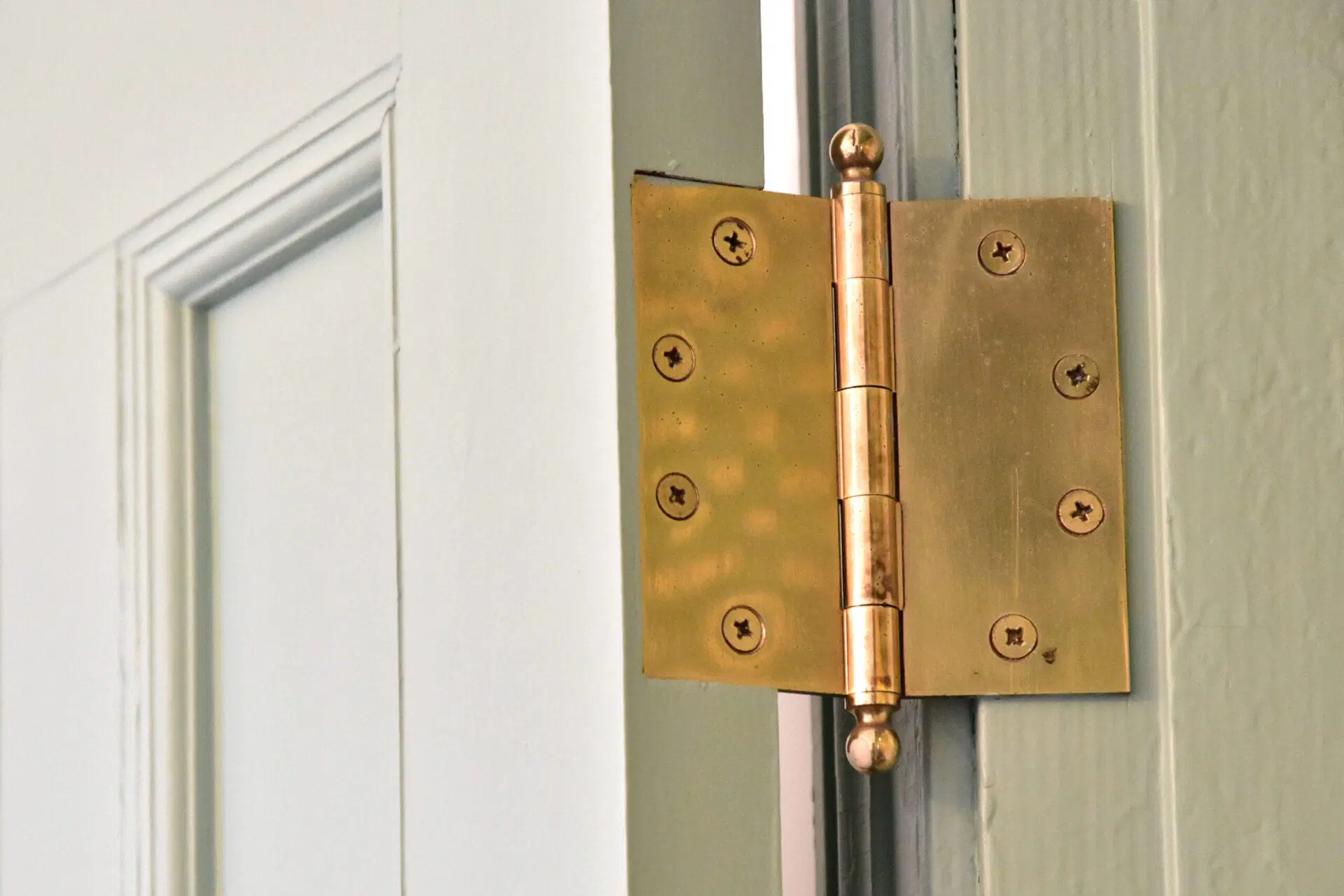 Close-up of a door hinge on a painted jamb with slightly backed-out screws and a screwdriver positioned to tighten them