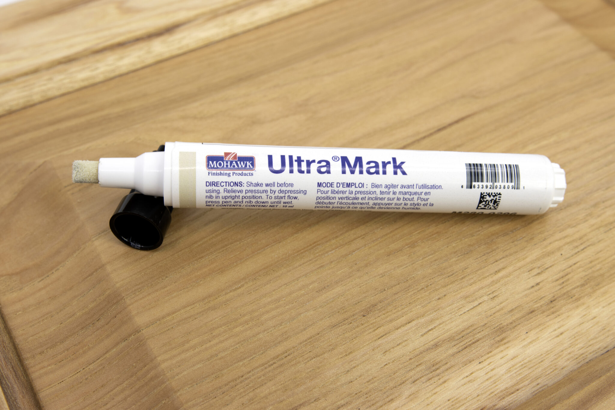 Close-up of a hand using a wood touch-up marker to color a thin scratch on a hardwood floor board