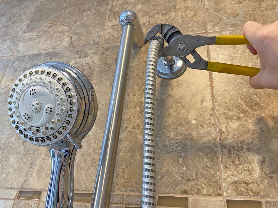 Close-up of an adjustable wrench gripping a showerhead nut with a cloth protecting the chrome finish while the showerhead is being loosened
