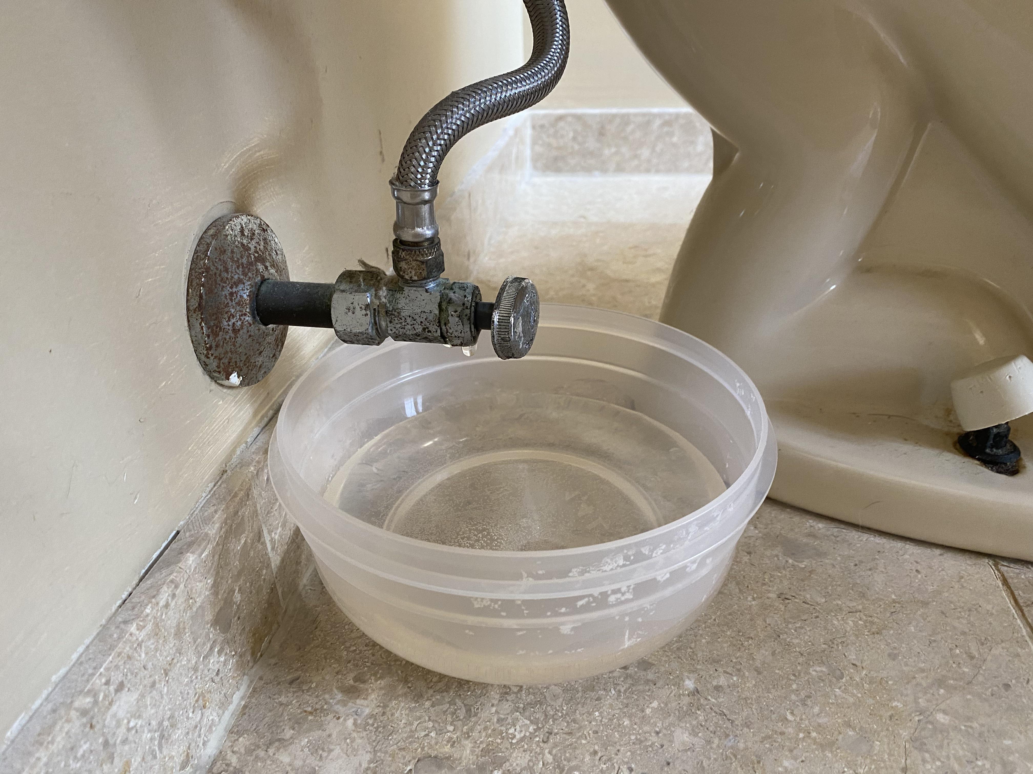 Close-up of an adjustable wrench tightening a compression nut on a copper shutoff valve under a kitchen sink
