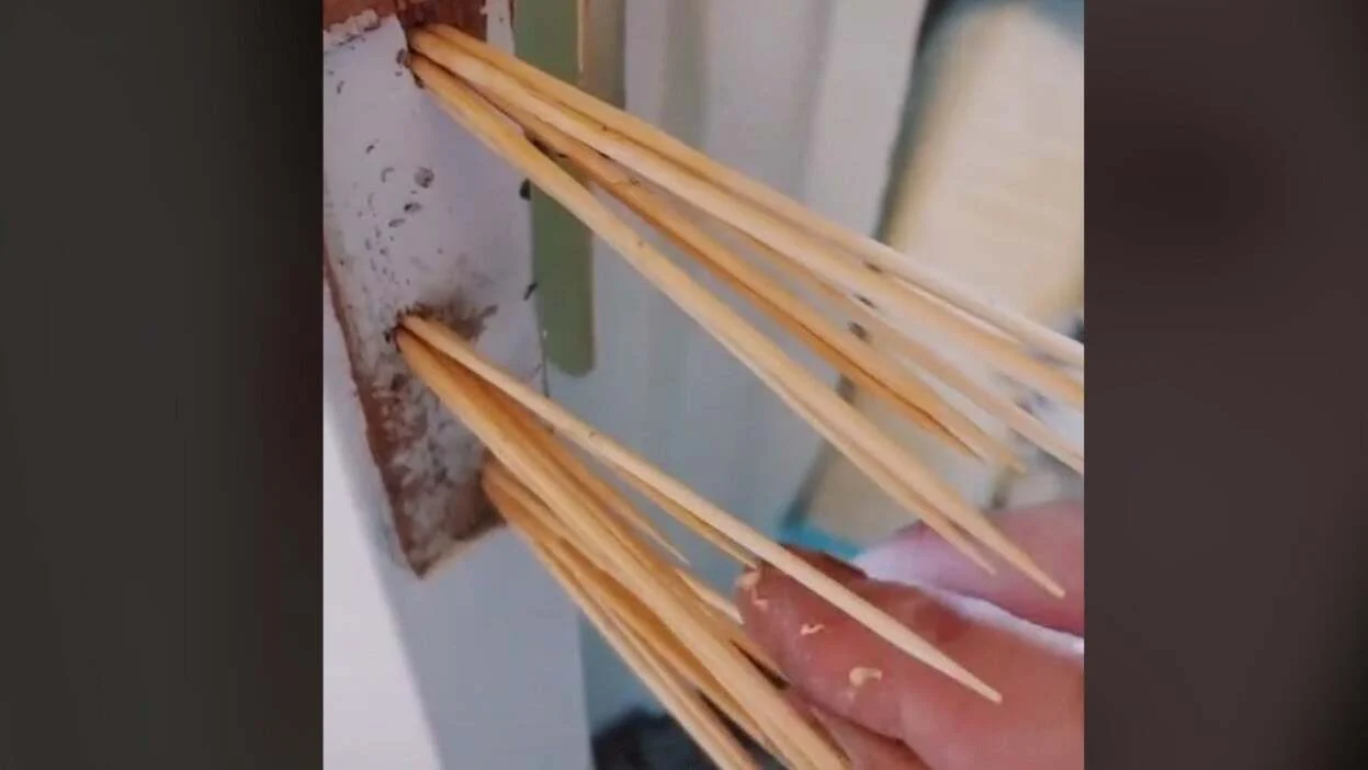 Close-up of toothpicks being inserted into a stripped screw hole in a wooden door frame with a small amount of wood glue visible