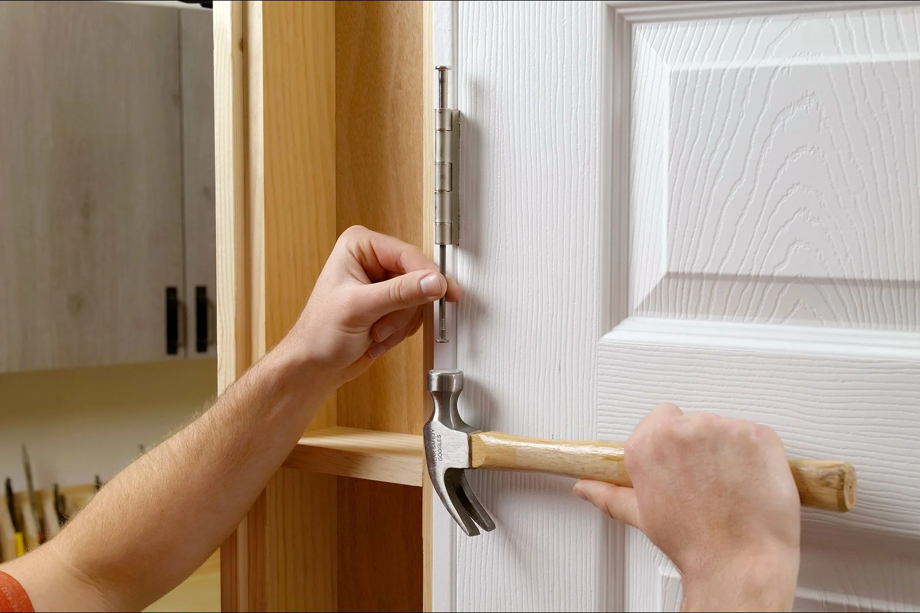 Closeup of a screwdriver and hammer tapping upward on the bottom of a door hinge pin to lift it out