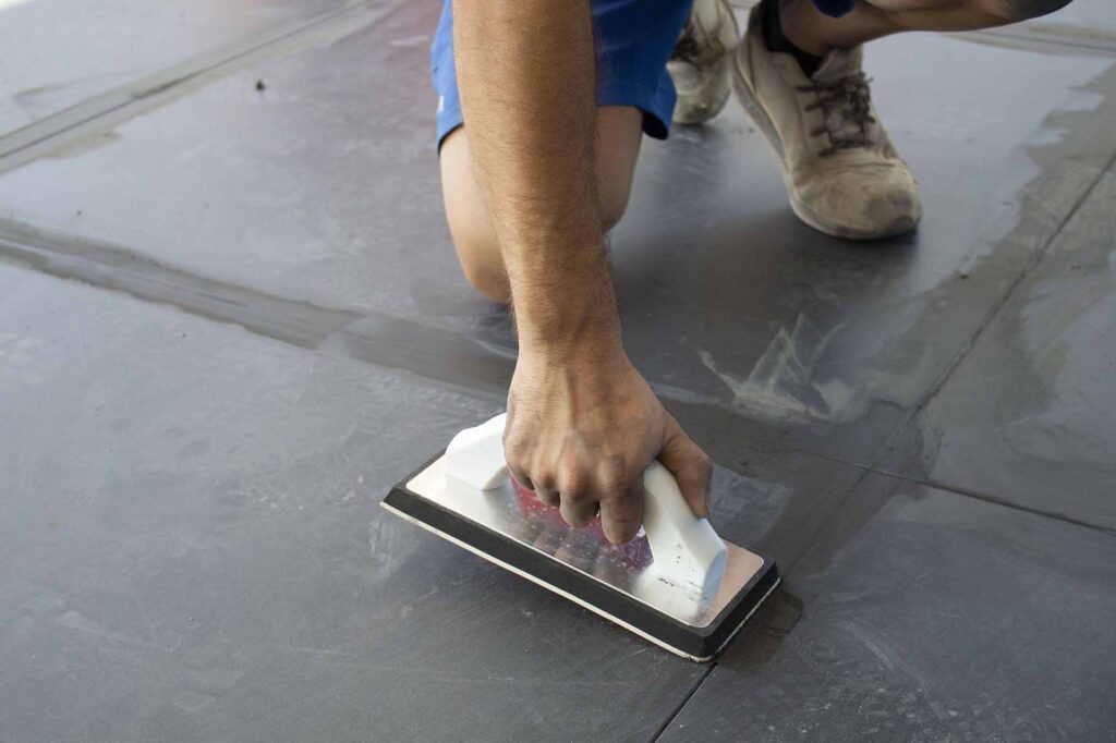 Grout being packed into joints around a newly installed tile with a rubber float