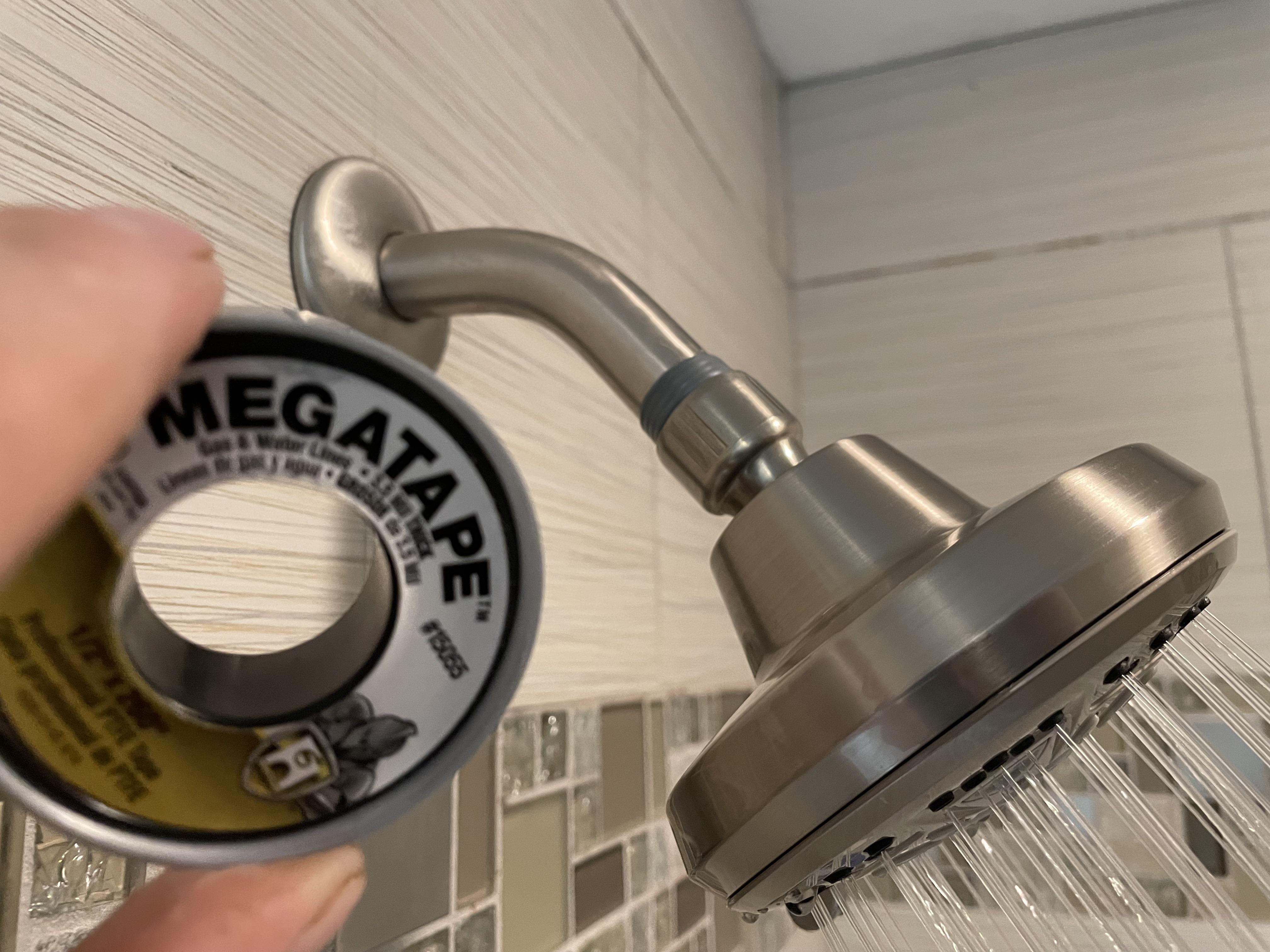 Hands wrapping white PTFE thread seal tape clockwise around the threads of a shower arm in a bathroom
