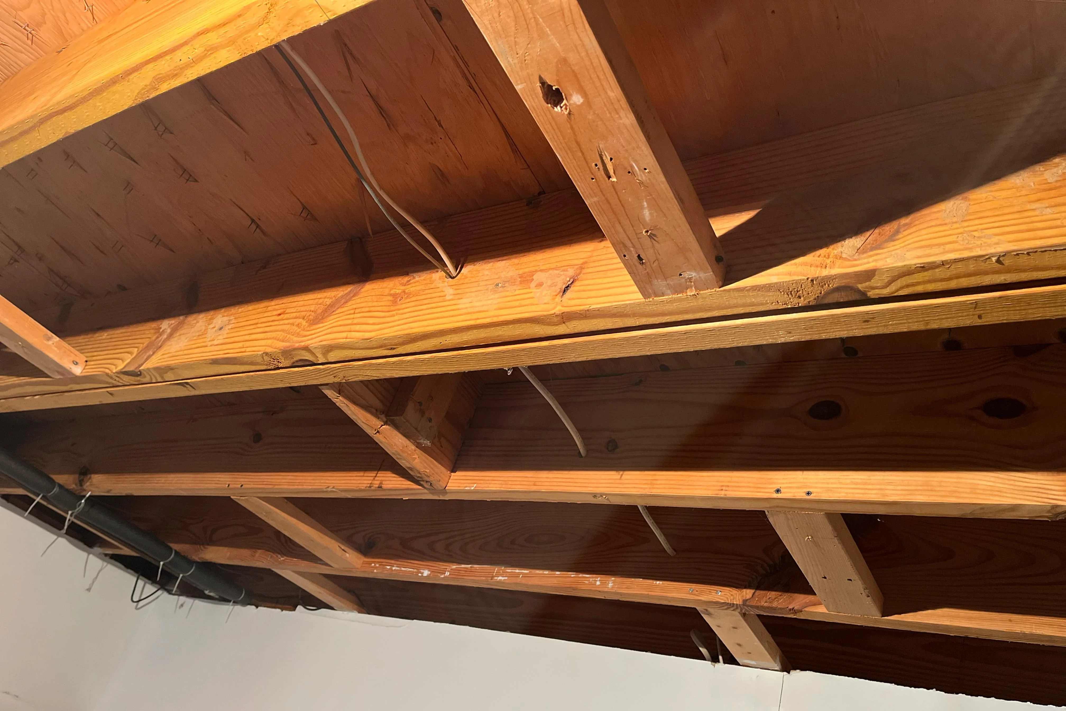In an unfinished basement, solid wood blocking installed between two floor joists with screws and adhesive squeeze-out visible