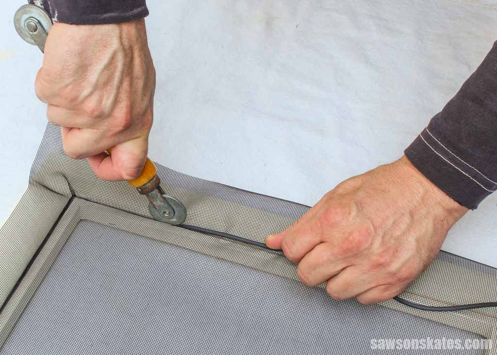Replacement window screen mesh laid over an aluminum screen frame on a workbench with excess mesh hanging over the edges