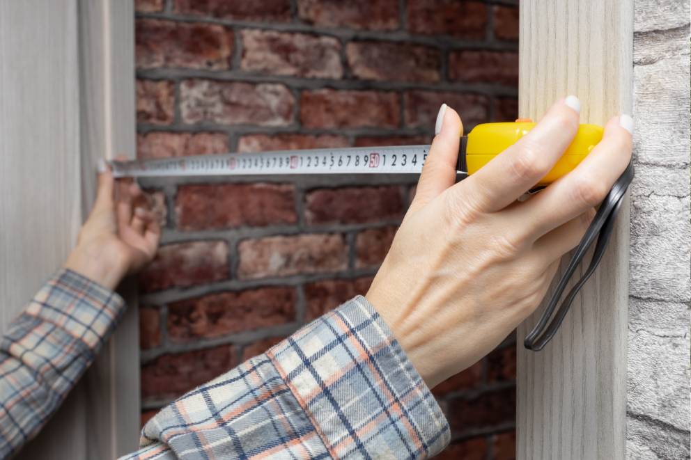 Tape measure stretched across the bottom edge of an exterior door to measure width for a replacement door sweep