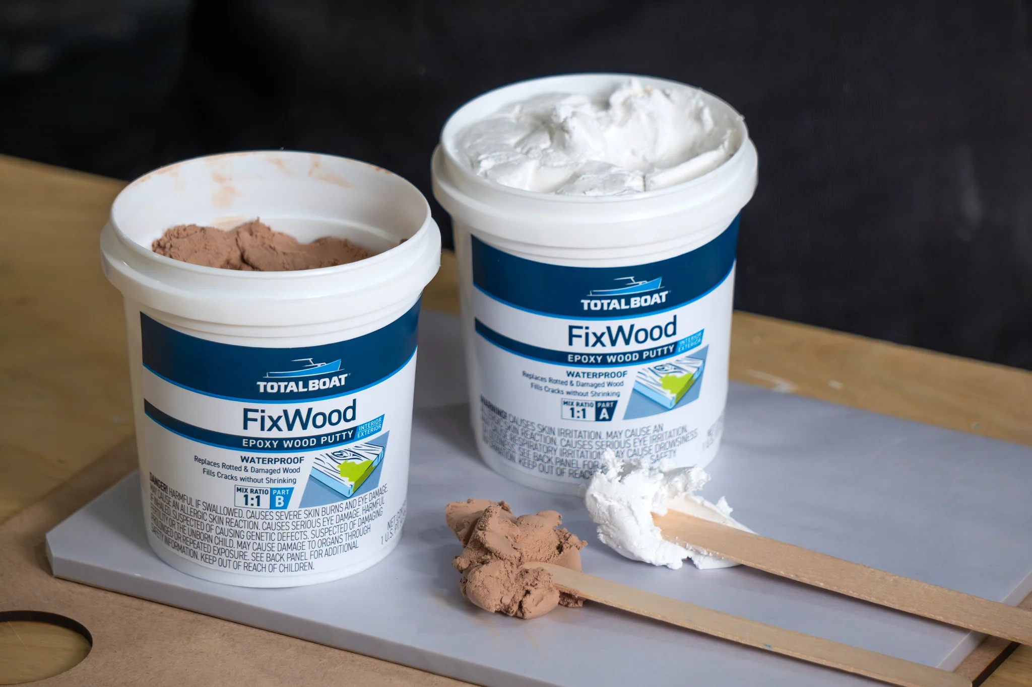 Two-part epoxy wood filler being mixed on a scrap board with a putty knife until the color is uniform